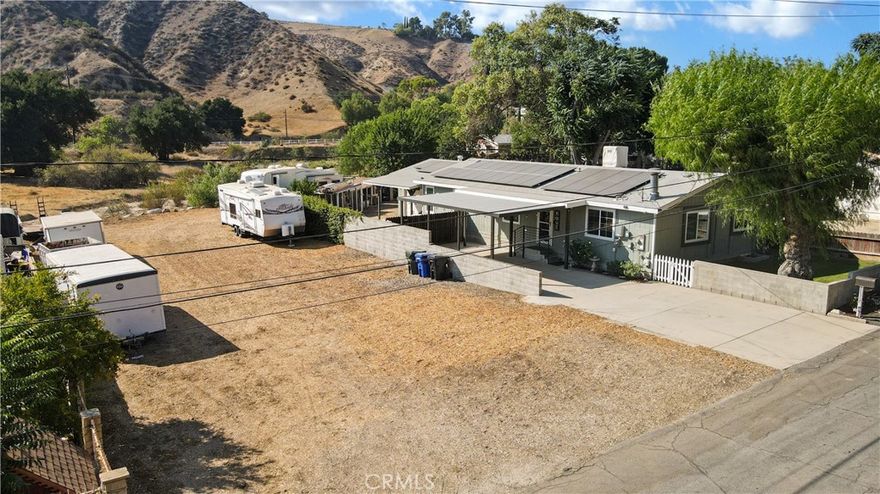 An updated and upgraded home with a extra wide residential lot awaits you. The front carport doubles as a patio and offers covered access to the front door. There is plenty of room for RV's, trucks and equipment on the lot. The home offers a totally remodeled (From the studs out) kitchen and dual pane windows throughout the house. The dining room has built in cabinetry with great storage space.  The primary suite has its own bath with a shower stall and separate large soaking tub. The primary bedroom windows offer a view down the canyon to the south. There is an indoor laundry room with its own outside access. The living room offers a free standing wood burning fireplace. Security cameras provide peace of mind across the entire lot. The attached 2 car garage has a built in work bench and there is a cozy office inside the garage with its own AC. At the rear is a fenced yard with chickencoops and a rear exit to the flat area behind the property that is an unused street easement. There are RV hookups at the lot rear that include water and electric access as well as waste disposal. Beyond that is a dry creek bed. The property is only 10 minutes from Valencia shopping, commercial, and medical service centers. The south side of the property has 2 separate vacant lots that could possibly be developed. The buyers should investigate all potential uses. Buyers are advised that the now closed Chiquita Canyon Landfill is within a mile of the subject property to the southeast. It was closed December 31, 2024.