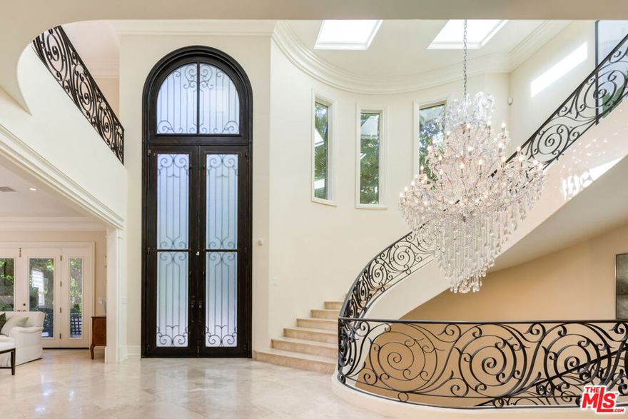 Tucked behind private gates and surrounded by lush, mature landscaping, this beautifully remodeled Tuscan retreat blends timeless elegance with modern sophistication. Beyond the manicured gardens, an impressive double-door entry opens to a grand double-height foyer adorned with an ornate chandelier and sweeping circular staircase. The formal living room flows effortlessly into the family room through French doors, creating an inviting space for both intimate gatherings and large-scale entertaining. The gourmet kitchen is a chef's dream, showcasing a generous center island with prep sink, custom cabinetry, and top-of-the-line appliances including a Wolf range, Sub-Zero refrigerator, and Miele espresso machine, warming drawers, and dishwasher. In the formal dining room, French doors open to Juliet balconies, filling the space with light and fresh canyon breezes. The expansive primary suite is a true sanctuary, featuring a private balcony, cozy fireplace, sitting area, dual custom walk-in closets, and a spa-inspired bath. Additional bedrooms are equally well-appointed, several with private balconies, while the home's many amenities include a pajama room, office, wine cellar, theater, and an impressive lower-level lounge ideal for billiards, music, or relaxation. Designed with wellness in mind, there is also a massage room, sauna, and steam shower. The resort-like backyard evokes the charm of a Mediterranean getaway with its cabana and outdoor living room, built-in barbecue, sparkling pool with European lion head fountains, spa with cascading waterfall, and numerous patios surrounded by terraced gardens. A tranquil front fountain completes this serene and private oasis, perfectly situated just moments from the heart of the city yet worlds away from it all.