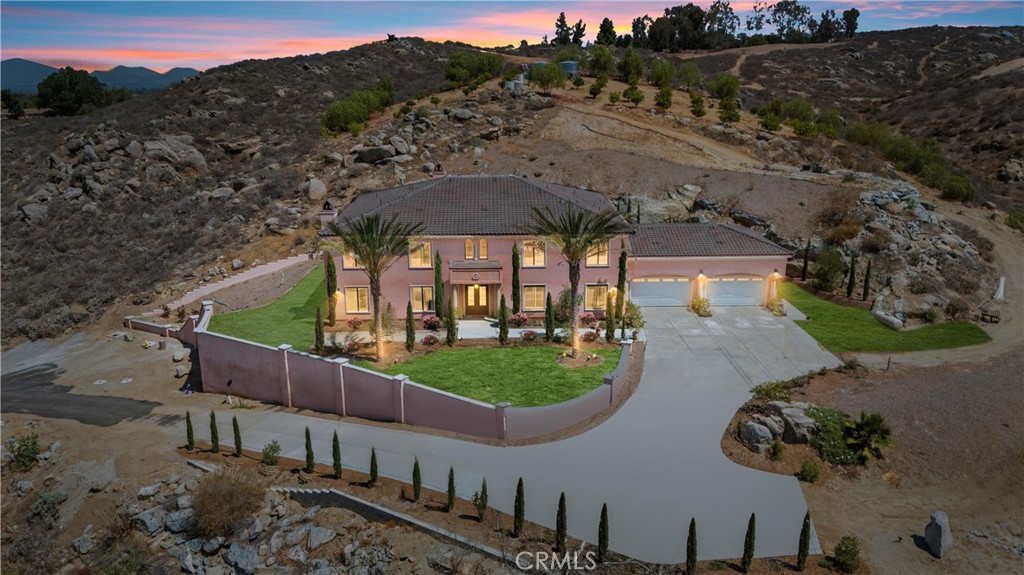 Nestled between Riverside’s prestigious Alessandro and Woodcrest communities, this Tuscan-inspired estate offers over 7,100 sq. ft. of refined living space with panoramic hillside views. Designed for both grand entertaining and intimate gatherings, the home showcases soaring coffered ceilings, elegant hardwood and tile floors, and an open floor plan that seamlessly connects multiple living and dining spaces. The gourmet chef’s kitchen is appointed with professional-grade appliances, an oversized walk-in pantry, and a butler’s kitchen for effortless hosting. Six spacious en-suite bedrooms include a grand primary retreat featuring a spa-style bath with soaking tub, dual vanities, and an oversized walk-in closet with its own laundry hookups for added convenience. Additional highlights include a private library, executive office, separate oversized laundry room, wide hallways, and a four-car garage with 25-foot ceilings and car lift capability to showcase custom cars or host private events. Built with sustainability and resilience in mind, the estate is equipped with two 1,000-gallon water tanks, two private fire hydrants, a custom four-tank septic system, and four 10-ton AC units. Outdoors, 2.44 acres of landscaped grounds feature mature citrus and olive trees, multiple patios, and expansive potential for a luxury pool, multigenerational ADU, or garden retreat all set against the scenic backdrop of the Riverside foothills. More than a residence, this is a legacy estate designed to be cherished for generations to come.