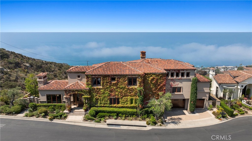 Nestled within a prestigious guard-gated community, this Mediterranean custom estate is perched on a scenic bluff, capturing sweeping, unobstructed views of the ocean, Catalina Island, and coastline from nearly every room. Thoughtfully designed with four bedrooms and a dedicated office, the residence features a sought-after main-level primary suite and ensuite baths in each bedroom, offering elevated comfort and privacy. Defined by timeless craftsmanship, the interiors blend rustic elegance with refined detail—highlighted by custom distressed wood beams, rich hardwoods, stone accents, and bespoke lighting throughout. French doors open to expansive viewing decks, creating a seamless connection to the coastal surroundings and inviting in ocean breezes. Tailored for both intimate gatherings and grand entertaining, the home offers a formal living room with stone fireplace, a sophisticated dining room, and a spacious great room that flows effortlessly into the chef’s kitchen. Culinary enthusiasts will appreciate the Thermador gas range with grill, double ovens, dual warming drawers, Sub-Zero refrigerator, and additional refrigerated drawers. A walk-in pantry, butler’s pantry, wet bar, and temperature-controlled wine room complete the entertainer’s experience. The outdoor living area offers a serene escape, enhanced by lush landscaping, a tranquil water feature, and a striking fireplace. This private retreat features the perfect backdrop for relaxed coastal living beneath the stars. All just moments from the renowned beaches, art galleries, and fine dining of Laguna Beach.
