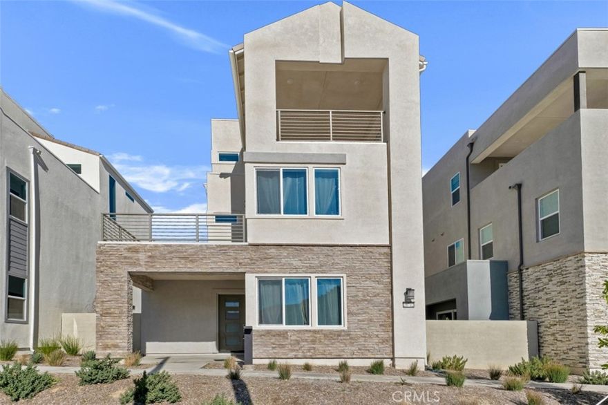 Set within the newly built Peak at Valencia enclave in the FivePoint Valencia neighborhood, this tri-level, light-filled, 4-bed, 3.5-bath, 2,843 sq ft contemporary residence showcases the appeal of modern new construction paired with unobstructed hillside views and a vibrant, amenity-rich community. The entry opens to a great-room style living space defined by high ceilings, recessed lighting, crisp finishes, and expansive windows that flood the home with natural light, while a textured wood accent wall adds warmth and architectural interest. The living, dining, and kitchen areas flow seamlessly together, with the dining space framed by floor-to-ceiling windows and the kitchen featuring an all-white palette, wide central island with seating for four, white shaker cabinetry, under-cabinet lighting, contemporary hardware, and built-in stainless-steel appliances. A main-level bedroom and full bath provide flexibility for guests or a home office. Upstairs, the spacious primary suite offers a private deck with contemporary railings and sweeping views of the surrounding hills, a generous walk-in closet, and a luxurious en-suite bath with dual-sink vanity, tile floors, and a glass-enclosed shower. 2 additional good-sized bedrooms share a full hall bath while a convenient laundry room completes the level. The upper living room serves as a versatile bonus area with bar, beverage refrigerator, and wine storage, and a convenient powder bath is ideal for a family room, office, studio, or play space, and opens through sliding glass doors to a California room/upper deck designed to maximize indoor-outdoor living. An attached two-car garage with direct access, EV charging, and storage adds everyday convenience. Residents enjoy access to three resort-style pools, playgrounds, parks, clubhouse facilities, and scenic walking trails, all within a fresh, thoughtfully planned community close to shopping, dining, and major attractions, including 6-Flags Magic Mountain, offering a lifestyle defined by newness, views, and effortless modern living.  Don’t miss your chance to join the neighborhood with this amazing home!