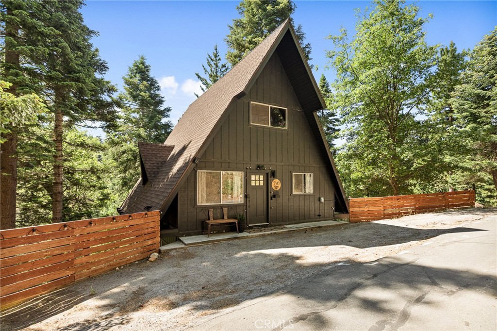 Tucked beneath the pines in beautiful Lake Arrowhead, this vintage 1970s A-frame cabin blends classic mountain character with tasteful updates. The exterior features the striking silhouette of a flat-faced prow, with its bold roofline, redwood fencing, and strong architectural lines that give this home standout presence. Inside, you’ll find soaring wood-beam ceilings and sunlight streaming through large triangular windows signature elements of the coveted prow-style design. A classic stone fireplace adds charm to the living area and connects naturally to the open dining space and thoughtfully updated kitchen, which includes open shelving and warm wood accents. Upstairs, a spacious loft-style game room offers flexibility for additional living space or recreation. The bathrooms have been beautifully updated with clean lines and modern finishes, thoughtfully designed to complement the home’s rustic touches. And just when you think it couldn't get better, the property also features a seasonal creek that adds to its serene charm, along with central AC to keep things cool and comfortable year round.
The outdoor deck provides space to enjoy the peaceful wooded surroundings, with mature trees and fresh mountain air creating a calming natural backdrop. This property also includes Lake Rights, giving owners access to Lake Arrowhead’s private amenities, including beaches, trails, and lake activities. Additional highlights include level-entry access a rare and sought-after feature in the area as well as a history of strong short-term rental performance. This well-maintained property offers a unique blend of mountain charm and modern comfort in one of Southern California’s most desirable alpine communities.