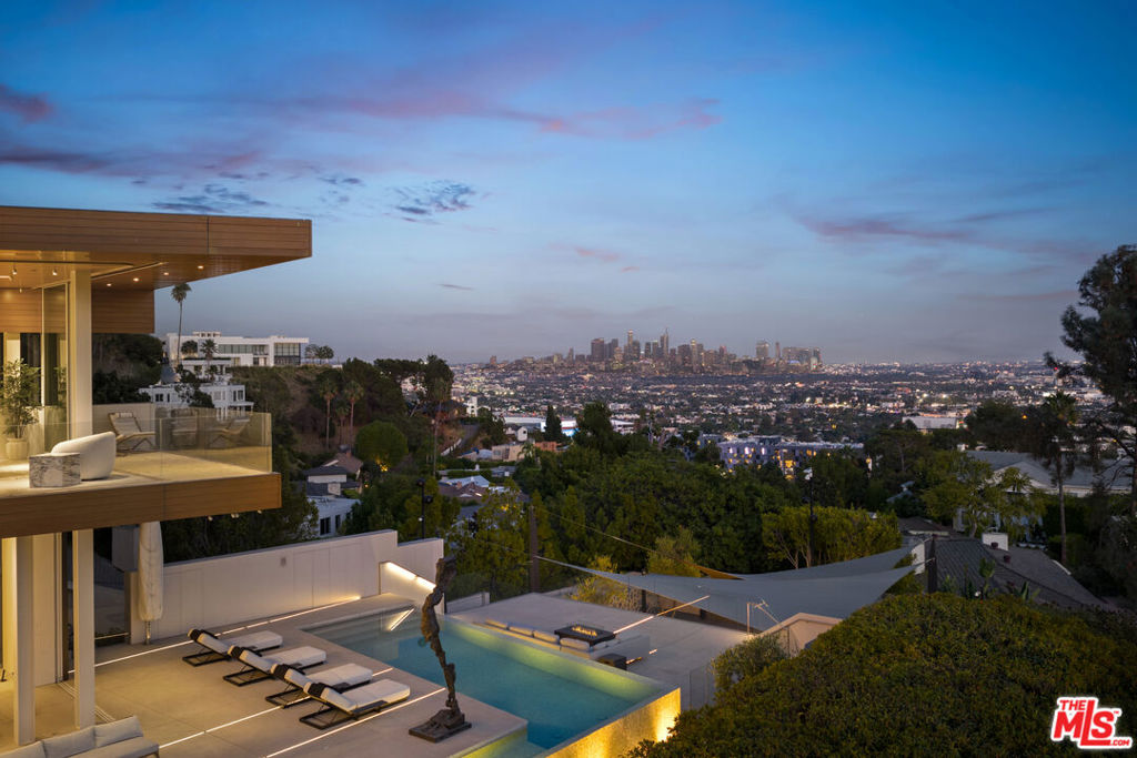 Hailed by Architectural Digest as a "sensational setting," this Sunset Plaza residence masterfully blends the visionary designs of McRitchie Design and Gary Hutton Design. Its striking steel-clad exterior opens to an interior of gallery-like elegance, balancing minimalist sophistication with a warm, inviting ambiance. Crafted to showcase art of any scale, the home features plywood-lined walls for seamless installations, complemented by radiant heated floors, a state-of-the-art security system, an elevator, and advanced smart home technology. Polished terrazzo floors, architectural lighting, and retractable glass walls accentuate both curated artwork and breathtaking views stretching from downtown to the Pacific Ocean. The open-concept layout seamlessly integrates a sleek, modern kitchen with the main living and dining areas, all flowing effortlessly onto an expansive sundeck featuring a custom mosaic-tiled pool and unobstructed vistas. Perched atop the residence, the glass-wrapped primary suite maximizes panoramic views, accompanied by three additional bedrooms, a luxurious media room, and a private outdoor deck. On the lower level, a versatile guest suite with its own bathroom and kitchen opens to a spacious covered deck, perfect for intimate gatherings or grand entertaining.
