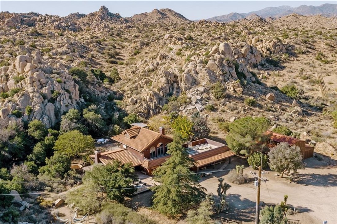 Welcome to Boulder Grove Ranch, an ultra-private 8+ acre estate carved into a secluded canyon of iconic boulders and sweeping desert vistas.
This design-forward compound features a sophisticated two-story main residence with a spacious primary suite and guest loft, plus a semi-detached guest house with its own private entrance. Elevated on the edge of two private boulder valleys, the property offers commanding views and a sense of quiet grandeur.
Curated interiors blend modern minimalism with rustic textures and bohemian warmth, creating a refined yet relaxed aesthetic. Purposefully reimagined as a luxury escape and part-time rental, Boulder Grove Ranch has hosted magazine-worthy weddings, high-end photo shoots, and intimate gatherings beneath the stars.
Amenities include a cedar soaking spa perched among the rocks, an architecturally striking barn and deck built into the boulders, and a network of trails and gathering spaces with artful signposts guiding you through the landscape.
Now eligible for wedding venue use with permit (buyer to verify), the estate offers exceptional potential for both lifestyle and income.
Secluded feeling yet a short 7 minute drive to Yucca Valley’s shops and dining, and easy access to Joshua Tree National Park & Palm Springs. Spanning three legal parcels and enveloping most of the surrounding cul-de-sac, this is a truly rare opportunity to own one of the High Desert’s most iconic private retreats.
