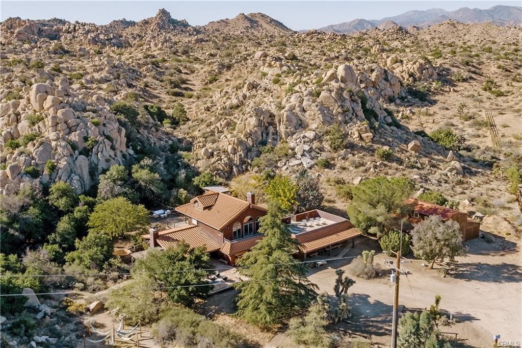 Welcome to Boulder Grove Ranch, an ultra-private 8+ acre estate carved into a secluded canyon of iconic boulders and sweeping desert vistas.
This design-forward compound features a sophisticated two-story main residence with a spacious primary suite and guest loft, plus a semi-detached guest house with its own private entrance. Elevated on the edge of two private boulder valleys, the property offers commanding views and a sense of quiet grandeur.
Curated interiors blend modern minimalism with rustic textures and bohemian warmth, creating a refined yet relaxed aesthetic. Purposefully reimagined as a luxury escape and part-time rental, Boulder Grove Ranch has hosted magazine-worthy weddings, high-end photo shoots, and intimate gatherings beneath the stars.
Amenities include a cedar soaking spa perched among the rocks, an architecturally striking barn and deck built into the boulders, and a network of trails and gathering spaces with artful signposts guiding you through the landscape.
Now eligible for wedding venue use with permit (buyer to verify), the estate offers exceptional potential for both lifestyle and income.
Secluded feeling yet a short 7 minute drive to Yucca Valley’s shops and dining, and easy access to Joshua Tree National Park & Palm Springs. Spanning three legal parcels and enveloping most of the surrounding cul-de-sac, this is a truly rare opportunity to own one of the High Desert’s most iconic private retreats.
