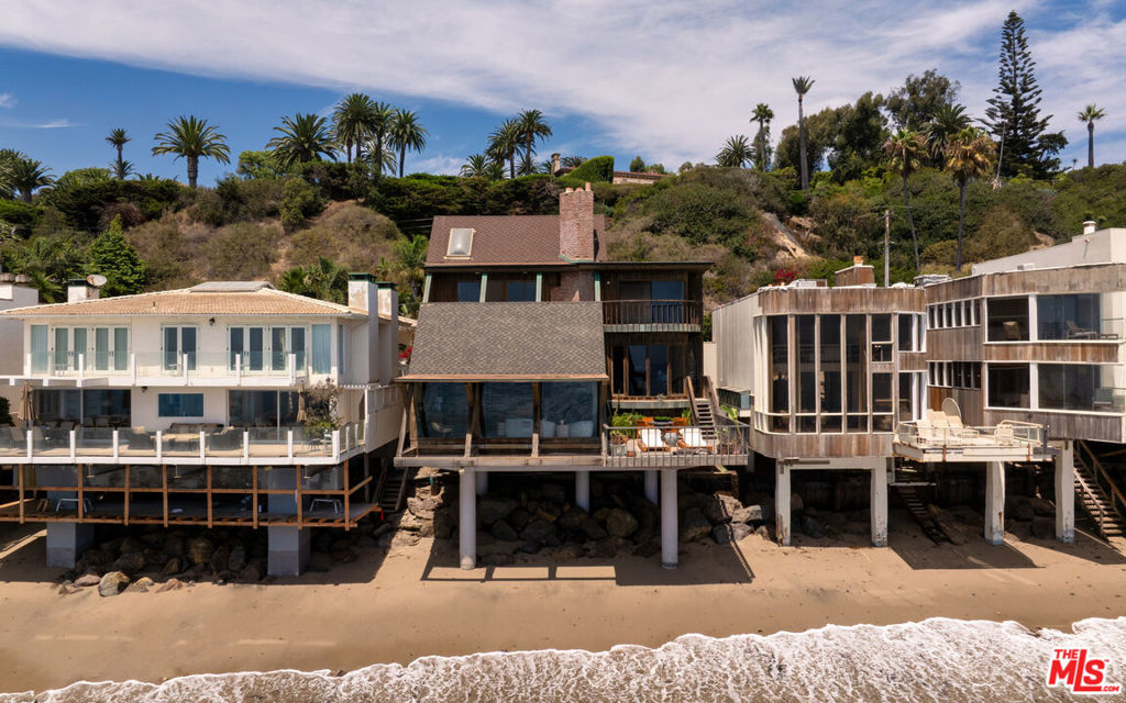 Poised on the quiet cul-de-sac end of Malibu Cove Colony's private road, this oceanfront estate is an extraordinary work of art by renowned architect Harry Gesner. With its soaring geometries, expressive woodwork, and walls of glass that frame the endless Pacific, the home reflects Gesner's signature blend of drama and intimacy. Approached by a wooden bridge detailed with nautical rope, the residence begins with monumental double doors salvaged from the historic San Francisco Mint, an entry that immediately signals rarity and provenance. Inside, a world of handcrafted artistry unfolds, illuminated by sunlight streaming through skylights and stained-glass windows reclaimed from a historic church. The interiors are a celebration of natural materials and timeless design. Wood-beam ceilings, wide-plank floors, and five fireplaces create warmth and character, while sweeping walls of glass open to panoramic views stretching down the coast to Point Dume. The main level embraces open concept living, where the family room flows seamlessly into a window-lined dining area and onward to an ocean-view kitchen featuring custom cabinetry, bar seating, a butcher block island, double Thermador ovens, and hand-tiled counters. On the level below, the living room serves as a dramatic gathering space with soaring ceilings, another grand brick fireplace, a stained-glass rose window, and sliding doors that open to a broad oceanfront deck designed for dining, lounging, and effortless indoor-outdoor living. Upstairs, three of the four bedrooms boast sweeping ocean views, capturing the artistry and serenity of this one-of-a-kind residence. The primary suite is a private sanctuary with wood beam ceilings, a fireplace with artisan tile detailing, and sliding doors to its own oceanfront balcony. A loft retreat, accessed by ladder, overlooks the coastline with extraordinary views. The primary bath continues the artistry with double vanities, a walk-in shower, an in-ground vintage tiled tub, and access to a second private terrace overlooking the lush hillside. Additional bedrooms feature sliding glass doors to ocean-view decks and stained-glass accents that enhance the home's singular character. Everywhere, bespoke craftsmanship abounds from custom built-ins to nautical-inspired railings underscoring the home's authenticity and artistry.With direct beach access and expansive decks hovering above the sand, this is more than a residence: it is a piece of California architectural history. A rare chance to own a Harry Gesner original in Malibu Cove Colony, where art, history, and coastal living converge in perfect harmony.