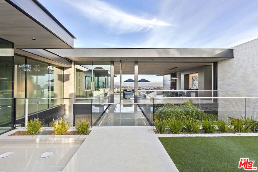 This striking, custom-built brand-new construction Paul McClean residence is located in the private and esteemed Trousdale Estates neighborhood. The home showcases approx. 10,500 square feet of clean lines and vaulted ceilings, with six ensuite bedrooms and nine total baths. A multitude of floor-to-ceiling casement windows encompass views of the canyon, mountains, downtown Los Angeles cityscapes and the Hollywood sign.  Amenities are all accounted for within the residence's design: a gym with a dry sauna and steam room, a movie theater with reclining seating for 10, a stunning aquarium with fish and coral, office, a wine bar and eight-car garage. The open chef's kitchen is built with Wolf appliances and an oversized marble island. A secondary back kitchen is designed for ease of catering/prep. The primary suite with a fireplace features stunning views overlooking the pool, canyon and city. Dual spacious closets and toilets in the primary bathroom as well as a large shower and stunning stone soaking tub. Outdoor features of the 19,614-square-foot lot include an infinity pool and spa, a heated loggia with outdoor dining and seating areas, a kitchen with a TV and bonus bathroom that all provide for easy and luxe open-air enjoyment. An architectural triumph, this sophisticated estate presents a truly elevated lifestyle experience in one of the most esteemed neighborhoods in Los Angeles.