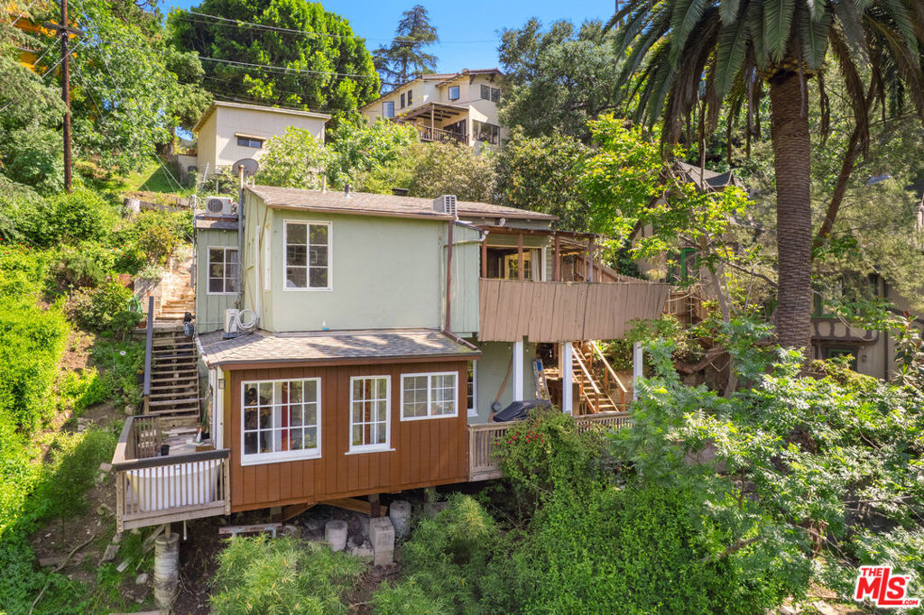 Tucked away just off Mulholland Drive, 6933 Vanland Trail is a character-rich hillside home with views out to the valley, mountains, and Hollywood sign offering the rare feeling of a secluded retreat while being moments from Studio City, the Hollywood Bowl, and the 101 freeway. Built by Kelsey Cook the storied "Sheriff of Hollywood" this unique property is one of only two homes he constructed on this peaceful trail, each filled with distinctive architectural charm and thoughtful use of space. Accessed via a stairway path, the property spans two levels: a 2-bedroom, 1-bathroom main residence above a full 1-bedroom, 1-bathroom guest unit below, complete with its own living room, kitchenette, loft, patio, work-from-home living, or hosting guests. Inside the main residence, you'll find vaulted wood-beam ceilings, large picture windows, and a floor-to-ceiling custom stone wall with a wood burning fireplace that anchors the living room. A wraparound deck extends the living space outdoors, offering treetop views and room for entertaining. The kitchen preserves its original cabinetry and includes a classic O'Keefe & Merritt stove a nod to the home's timeless design. The lower unit features a newly renovated bathroom, a freestanding soaking tub on the deck, and a mini-split system in the bedroom for year-round comfort. Several outdoor entertaining areas are thoughtfully layered across the property, taking full advantage of the deep lot and surrounding natural beauty. A one-of-a-kind residence with rich character, and true versatility all in a quiet canyon setting just minutes from the pulse of LA.