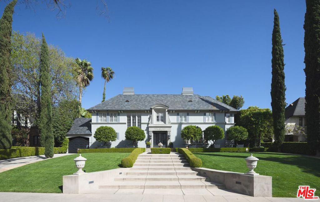 Stunning significant gated Traditional Hancock Park Estate set on elevated 26,000+ square feet of extraordinary private grounds. Masterfully redone and designed by renowned Brian Little with tremendous attention to detail featuring classic and timeless elements in every aspect. Beautiful entry, gracious living room with oversized fireplace and coffered ceiling details. Wood paneled library with fireplace, an office/study with built in cabinetry, formal dining room with perfect scale, chefs gourmet kitchen with center island, top appliances, breakfast area all opens to family room with fireplace and French doors opening to gardens. Great for entertaining as all primary rooms open to the stone terraces and gardens and expansive lawn. The 2nd floor features a primary suite wing with sitting room, view terrace overlooking the grounds, gorgeous bath and walk in closet/dressing room. 3 additional en suite family bedrooms each with beautiful details and one with a bonus/optional 5th bedroom area. Large accessible 3rd floor attic can be expansive closet space/storage. The basement provides adequate space for wine cellar, theatre and storage. The property has an amazing extra-large guest house structure matching the main house in architectural design. A long-gated driveway leads through the Porte-cochere to a rear motor court with extra parking and 2 custom garages. The self-contained guest house has a full kitchen, living room with fireplace and 2 bedrooms. In addition, there is a gym, bathroom (and outdoor shower) and a covered pool lounge area with fireplace. Gardens include specimen trees, sculpted hedgerows, roses, fountains, play areas, full outdoor kitchen, large swimmers pool and spa with cover. Don't miss this one of a kind opportunity to acquire this rare and immaculate Estate!