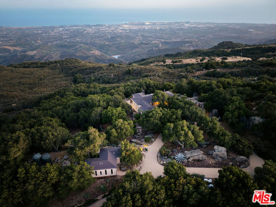 Set on 6.29 acres between Windemere Ranch and the Los Padres National Forest, this serene estate offers unmatched privacy and panoramic views converge in a setting that feels worlds away, yet is just 20 minutes from town. Completed in 2011, the thoughtfully conceived mini-compound is a masterclass in architectural harmony with the land. The 2 BD/2BA main house is designed to integrate seamlessly with the dramatic vertical rock outcroppings, with a second, standalone 2BD/1BA set in a tranquil pastoral setting offering additional comfort and flexibility. Enjoy private trails, an ocean-view pool, outdoor fireplace, and a producing orchard. A rare sanctuary immersed in nature's beauty. This is not just a property, it's a lifestyle of intentional living, immersed in the rhythms of nature.A Hidden Sanctuary of Privacy, Beauty, and Comfort Set in NatureDiscover the rare serenity of this captivating 6.29-acre (+/-) estate, where unmatched privacy and panoramic views converge in a setting that feels worlds away, yet is just 20 minutes from shopping, dining, and everyday conveniences.Nestled between the untouched expanse of the Los Padres National Forest and the renowned Windemere Ranch, this exceptional property is truly immersed in the embrace of nature. Completed in 2011, the thoughtfully conceived mini-compound is a masterclass in architectural harmony with the land. Designed to integrate seamlessly with the dramatic vertical rock outcroppings, the property offers a sense of sanctuary and wonder at every turn.The main two bedroom, two bathroom residence is positioned to capture sweeping vistas of the Santa Barbara coastline. Expansive, vanishing glass walls dissolve the boundaries between inside and out, inviting the Pacific, Channel Islands, and city lights into the home and creating a seamless indoor-outdoor lifestyle. Whether it's taking in the golden glow of sunset on the terrace by the outdoor fireplace, or enjoying coffee in the soft mist of morning, every moment here is framed in natural beauty.A second, standalone residence offering two bedrooms, one bathroom, and a kitchenette, features an equally stunning vantage point-complete with ocean views set in a tranquil pastoral setting. Ideal for hosting guests, extended family, or serving as a sophisticated work-from-home retreat, this secondary dwelling enhances the property's flexibility and appeal and is far enough from the main home for desired separation.The grounds are nothing short of enchanting. Wander through private trails shaded by native oaks, and soaring stone monoliths. Take a revitalizing swim in the ocean-view pool, or simply relax in the profound stillness that surrounds you. An orchard features numerous citrus, fruit, and avocado trees.This is not just a property, it's a lifestyle of intentional living, immersed in the rhythms of nature.Privacy. Luxury. Peace. Nature. This is your own piece of paradise, rarely available, and never to be replicated.