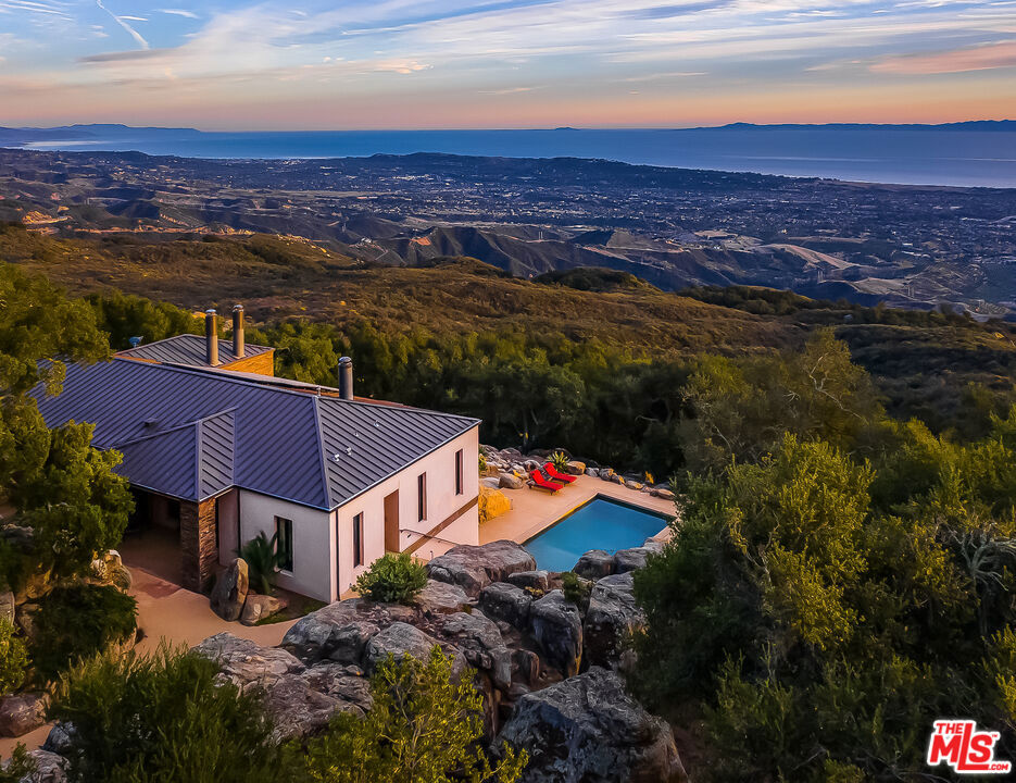 Set on 6.29 acres between Windemere Ranch and the Los Padres National Forest, this serene estate offers unmatched privacy and panoramic views converge in a setting that feels worlds away, yet is just 20 minutes from town. Completed in 2011, the thoughtfully conceived mini-compound is a masterclass in architectural harmony with the land. The 2 BD/2BA main house is designed to integrate seamlessly with the dramatic vertical rock outcroppings, with a second, standalone 2BD/1BA set in a tranquil pastoral setting offering additional comfort and flexibility. Enjoy private trails, an ocean-view pool, outdoor fireplace, and a producing orchard. A rare sanctuary immersed in nature's beauty. This is not just a property, it's a lifestyle of intentional living, immersed in the rhythms of nature.A Hidden Sanctuary of Privacy, Beauty, and Comfort Set in NatureDiscover the rare serenity of this captivating 6.29-acre (+/-) estate, where unmatched privacy and panoramic views converge in a setting that feels worlds away, yet is just 20 minutes from shopping, dining, and everyday conveniences.Nestled between the untouched expanse of the Los Padres National Forest and the renowned Windemere Ranch, this exceptional property is truly immersed in the embrace of nature. Completed in 2011, the thoughtfully conceived mini-compound is a masterclass in architectural harmony with the land. Designed to integrate seamlessly with the dramatic vertical rock outcroppings, the property offers a sense of sanctuary and wonder at every turn.The main two bedroom, two bathroom residence is positioned to capture sweeping vistas of the Santa Barbara coastline. Expansive, vanishing glass walls dissolve the boundaries between inside and out, inviting the Pacific, Channel Islands, and city lights into the home and creating a seamless indoor-outdoor lifestyle. Whether it's taking in the golden glow of sunset on the terrace by the outdoor fireplace, or enjoying coffee in the soft mist of morning, every moment here is framed in natural beauty.A second, standalone residence offering two bedrooms, one bathroom, and a kitchenette, features an equally stunning vantage point-complete with ocean views set in a tranquil pastoral setting. Ideal for hosting guests, extended family, or serving as a sophisticated work-from-home retreat, this secondary dwelling enhances the property's flexibility and appeal and is far enough from the main home for desired separation.The grounds are nothing short of enchanting. Wander through private trails shaded by native oaks, and soaring stone monoliths. Take a revitalizing swim in the ocean-view pool, or simply relax in the profound stillness that surrounds you. An orchard features numerous citrus, fruit, and avocado trees.This is not just a property, it's a lifestyle of intentional living, immersed in the rhythms of nature.Privacy. Luxury. Peace. Nature. This is your own piece of paradise, rarely available, and never to be replicated.