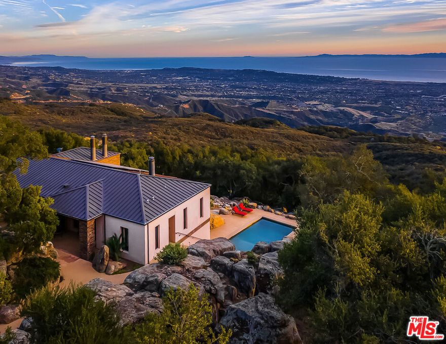 Set on 6.29 acres between Windemere Ranch and the Los Padres National Forest, this serene estate offers unmatched privacy and panoramic views converge in a setting that feels worlds away, yet is just 20 minutes from town. Completed in 2011, the thoughtfully conceived mini-compound is a masterclass in architectural harmony with the land. The 2 BD/2BA main house is designed to integrate seamlessly with the dramatic vertical rock outcroppings, with a second, standalone 2BD/1BA set in a tranquil pastoral setting offering additional comfort and flexibility. Enjoy private trails, an ocean-view pool, outdoor fireplace, and a producing orchard. A rare sanctuary immersed in nature's beauty. This is not just a property, it's a lifestyle of intentional living, immersed in the rhythms of nature.A Hidden Sanctuary of Privacy, Beauty, and Comfort Set in NatureDiscover the rare serenity of this captivating 6.29-acre (+/-) estate, where unmatched privacy and panoramic views converge in a setting that feels worlds away, yet is just 20 minutes from shopping, dining, and everyday conveniences.Nestled between the untouched expanse of the Los Padres National Forest and the renowned Windemere Ranch, this exceptional property is truly immersed in the embrace of nature. Completed in 2011, the thoughtfully conceived mini-compound is a masterclass in architectural harmony with the land. Designed to integrate seamlessly with the dramatic vertical rock outcroppings, the property offers a sense of sanctuary and wonder at every turn.The main two bedroom, two bathroom residence is positioned to capture sweeping vistas of the Santa Barbara coastline. Expansive, vanishing glass walls dissolve the boundaries between inside and out, inviting the Pacific, Channel Islands, and city lights into the home and creating a seamless indoor-outdoor lifestyle. Whether it's taking in the golden glow of sunset on the terrace by the outdoor fireplace, or enjoying coffee in the soft mist of morning, every moment here is framed in natural beauty.A second, standalone residence offering two bedrooms, one bathroom, and a kitchenette, features an equally stunning vantage point-complete with ocean views set in a tranquil pastoral setting. Ideal for hosting guests, extended family, or serving as a sophisticated work-from-home retreat, this secondary dwelling enhances the property's flexibility and appeal and is far enough from the main home for desired separation.The grounds are nothing short of enchanting. Wander through private trails shaded by native oaks, and soaring stone monoliths. Take a revitalizing swim in the ocean-view pool, or simply relax in the profound stillness that surrounds you. An orchard features numerous citrus, fruit, and avocado trees.This is not just a property, it's a lifestyle of intentional living, immersed in the rhythms of nature.Privacy. Luxury. Peace. Nature. This is your own piece of paradise, rarely available, and never to be replicated.
