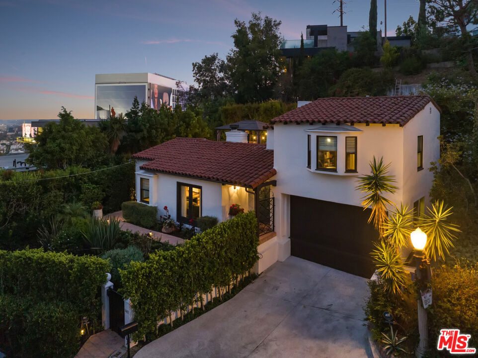 In a colorful garden setting just a few doors above Sunset, this vintage 2-story Spanish Revival home is ideally located in the heart of the Strip, close to many great dining establishments, upscale hotels, the Sunset Plaza shopping district, and West Hollywood's most happening nightlife. As you approach the gated home, you'll be charmed by the lush, vibrant landscaping. Enter through the original paneled front door and be welcomed by the arched walls, warm oak floors, and coved plaster ceilings laid out in a classic floor plan that incorporates large private patios on both the first and second levels; it's a California lifestyle classic. Many French doors bring great light into the interiors, and the original fireplace imbues the home with a warm, classic ambiance. The dining room, perfect for dinner parties, opens to a very private courtyard through a wall of glass doors. A previous renovation transformed the garage into a spacious primary suite, complete with a built-in wall of wardrobe cabinets and a beautiful white marble bathroom. Upstairs is a second white mosaic marble bathroom with tub and shower, and two more bedrooms; both are light-filled, one with two large closets and French doors that open to a patio that features a covered gazebo with TV entertainment system. Enjoy the glamor and excitement of the iconic Sunset Strip while living in a light-filled classic home in a private green garden; complete privacy just moments away from great experiences.