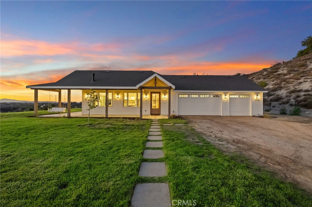 Experience the charm of country life in this custom single story modern farmhouse set on 10 acres with panoramic views in the heart of Temecula Wine Country. Built just two years ago, this home blends timeless farmhouse design with contemporary comfort and sustainable, off grid living. From its inviting wraparound porch to its vaulted ceilings and warm white wood interior, every detail reflects quality and craftsmanship. The open floor plan welcomes abundant natural light and showcases sweeping vineyard valley views from the main living areas. The chef’s kitchen is a showstopper featuring a 48” cooktop, double ovens, farmhouse sink, walk in pantry, and an oversized quartz topped island perfect for entertaining. The living and dining areas flow seamlessly together, anchored by a cozy fireplace and plenty of room for gatherings. The primary suite offers private exterior access, breathtaking views, and its own fireplace. A spa style bath includes a soaking tub, walk in shower, dual vanities, and a spacious walk in closet. Three additional bedrooms, two full baths, a home office or flex room, and a large laundry room complete the thoughtful layout. An attached oversized three car garage with pull through design provides ample space for vehicles, RVs, and recreational equipment. Designed for energy independence, the home features 44 solar panels, 2 batteries, 3 inverters and a backup generator, allowing for true off grid capability. For added versatility or investment potential, the property includes a 680 sq ft ADU with two 1 bed, 1 bath units, each with its own kitchen, living area, and private entrance. Perfect for extended family, guests or rental income opportunities. With no HOA, there’s room to bring animals, add a pool, barn, or workshop. The options are endless. Just minutes from Temecula’s wineries, shopping, dining, and top schools, this property delivers the best of both worlds: peaceful Wine Country living with modern convenience. Discover your forever home and experience sustainable country living at its finest.