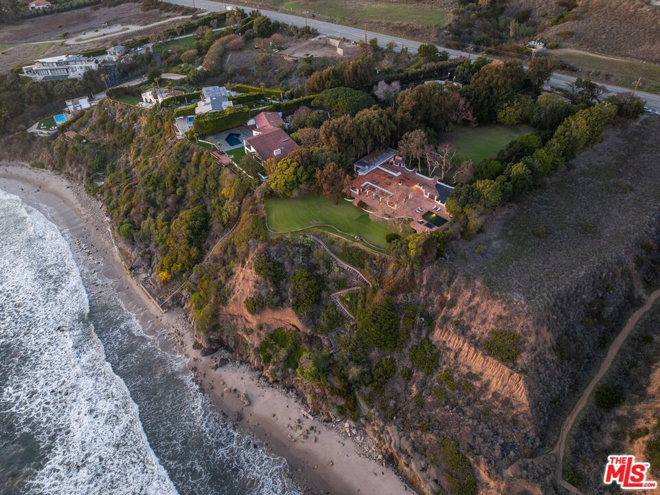 Presenting one of the largest and most impressive oceanfront parcels ever offered in Malibu, this sprawling, mostly flat 2.6-acre estate offers unparalleled grandeur, privacy, and natural beauty. Majestic views stretch across Point Dume, Palos Verdes, distant islands, and the shimmering coastline, framed by mature trees and meticulously manicured lawns that capture endless sunsets. Nestled on the serene Encinal Bluff, this rare parcel boasts exclusive beach access down a private stairway and over 75 feet of lush, grassy oceanfront lawn, a perfect blend of seclusion and coastal splendor. Included are fully approved City of Malibu permits and architectural plans by renowned designer Richard Landry for a new 7,912-square-foot, five-bedroom, seven-bath estate. The existing residence, a quintessential California Spanish-style masterpiece, sits at the end of a long, tree-lined driveway, exuding timeless elegance. Designed for seamless indoor-outdoor living, this single-level home features soaring ceilings with exposed beams, expansive windows, Saltillo tile, hardwood floors, exquisite cabinetry, and signature Malibu tile accents. The main house includes four bedrooms, highlighted by a luxurious primary suite with its own fireplace, walk-in closet, beautifully tiled bath, and private backyard entry. A separate guest house, thoughtfully designed with three bedrooms, two-and-a-half baths, a living room, dining area, kitchen, and laundry, adds versatility and comfort. This iconic property stands as one of Western Malibu's most coveted treasures, blending rare scale, architectural pedigree, and an unrivaled coastal setting.