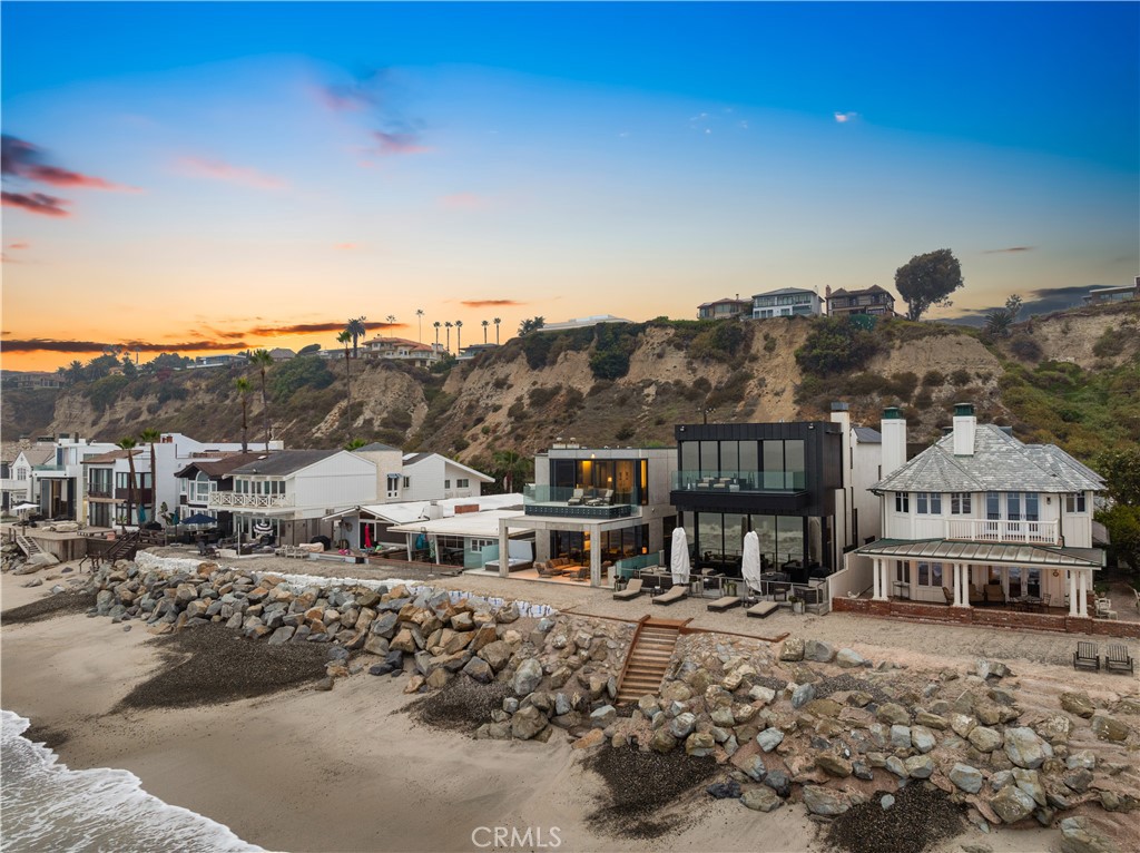 Standing directly on the sand along Capistrano Beach's exclusive guard-gated Beach Road community in
Dana Point, this extraordinary custom home pairs stunning modern architecture with panoramic ocean,
beach, Catalina Island, sunset, whitewater and coastline views. Natural wood, patinated copper, glass, metal
and concrete combine to distinguish exterior architecture that is destined to stand the test of time. Designed
by Mark Singer and built by Crawford Custom Homes with an interior by Terry Hunziker, the spacious, open
and light two-story residence is truly a seaside oasis that showcases a soaring double-height entry, open-
concept living spaces, and a bespoke selection of top-tier finishes and fixtures throughout approximately
3,503 square feet. Five bedrooms and five baths include four luxurious ensuites and a main-level bedroom
that is perfect for guests. Opening via a wall of Arcadia glass doors to a covered beachfront patio with spa
and built-in BBQ, the living room, dining room and kitchen form one seamless space that generously
accommodates impressive entertaining and easy daily living. A custom entertainment wall with linear
fireplace and surround sound anchors the living room, and the kitchen displays a large island with seating,
sleek European-style frameless cabinetry, open shelving, leathered quartzite countertops, and a custom
backsplash with built-in storage and a unique in-wall spice organizer. Chefs of every skill level will benefit
from top-of-the-line appliances that include a built-in cabinet-matched Miele refrigerator, built-in ice-maker,
and a drawer microwave and versatile multi-burner cooktop from Gaggenau. Ascend a dramatic floating
staircase to the second level of this peerless beachfront home, where floor-to-ceiling windows welcome
natural light, and a lavish primary suite overlooks the sand, breaking waves and Pacific Ocean while
revealing a deck, freestanding tub, separate shower, floating vanities, and a walk-in closet with custom built-
in cabinets. Concrete walls, wood-plank ceilings, chic lighting and custom built-ins are featured in select
areas, and radiant-heat flooring, Crestron home automation, a two-car garage, three parking spaces and
storage across the street, and a built-in back-up generator elevate preferred living. Residents of Beach Road
enjoy a private beach extending nearly 1.5 miles that is close to Dana Point’s harbor and Lantern District, and biking, hiking and walking trails.