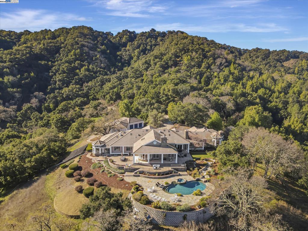 Nestled in the scenic Pleasanton Ridge, this 77.48-acre estate offers unmatched luxury and privacy. Built in 2000, the custom home spans 8,590 square feet with a single-level layout featuring seven bedrooms, six full baths, and two half baths. The gourmet kitchen is equipped with high-end appliances, stone countertops, and a breakfast bar, ideal for both everyday meals and entertaining. The adjacent family room boasts a cozy gas fireplace and large windows framing stunning views of Mt. Diablo and the valley. The expansive primary suite includes a spa-like bathroom with a jetted tub, stall shower, and skylight, plus a private retreat for quiet moments or a home office. A laundry room completes the main level. A highlight of this estate is the 10-car, museum-quality garage with heating, air conditioning, checkered flooring, and central vacuum. With 4 additional car garages provide extra storage and convenience. Outside, the landscaped grounds feature a swimming pool, a spacious deck, and a patio perfect for alfresco dining, all with panoramic views of the valley. This exceptional estate offers the ultimate in luxury, comfort, and natural beauty. Located in a top-rated school district, it provides excellent education for your children while offering a serene, outdoor lifestyle.