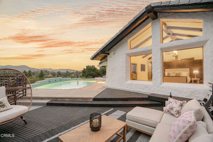 Perched well above street level and set behind a long driveway, this custom home has been refined with contemporary styling and offers unforgettable views and extreme privacy in idyllic Westlake Trails. A grand double-door entry opens to large, bright living spaces with wood floors, high-beam ceilings and an abundance of oversized windows flooding the home with tons of natural light and showcasing spectacular views throughout. The step-down living room offers views, a sleek fire feature and an adjacent wet-bar with Carrera marble and counter seating. The gorgeous kitchen is generously equipped with glass-front shaker cabinetry, Carrara marble counters and backsplash, a large island and high-end appliances including a built-in wine fridge and espresso machine. The open layout flows into a family room with a beautiful floor-to-ceiling tiled fireplace, more oversized windows and balcony access connecting a beautiful interior space with views of the Conejo Valley. This home offers two generously sized bedroom suites; one on the main level and one on the lower level, creating privacy and versatility for usage. In addition, a spacious loft with en-suite bath, walk-in closet and private balcony offers the flexibility to be used as a fabulous 4th bedroom suite, dedicated office space or other creative space. The sizable primary suite captures stunning views with a high wall of windows and a glass door accessing the pool, spa and outdoor lounging spaces. The high beam ceiling, modern chandelier and wooden feature wall add modern character to this sophisticated retreat. The en-suite bathroom is spacious and finished with dark stone, oversized shower, floating dual vanity, separate water closet, walk-in closet and more incredible views. Outside, the panoramic Conejo Valley views are a show-stopper in the rear yard. Relax and lounge on the patio, one of the multiple balconies or in the pool/spa surrounded by breathtaking views. Out front, a three-car garage and massive, long driveway provide ample parking or extra play space. A majestic oak tree is a perfect complement to the property, offering shade and a touch of whimsy with swings swaying gently beneath huge, twisting branches. Sweeping panoramic views, exceptional privacy and freshly redesigned with contemporary styling, this incredible custom home is a private haven perfectly situated in one of the most sought-after neighborhoods of Westlake Village.