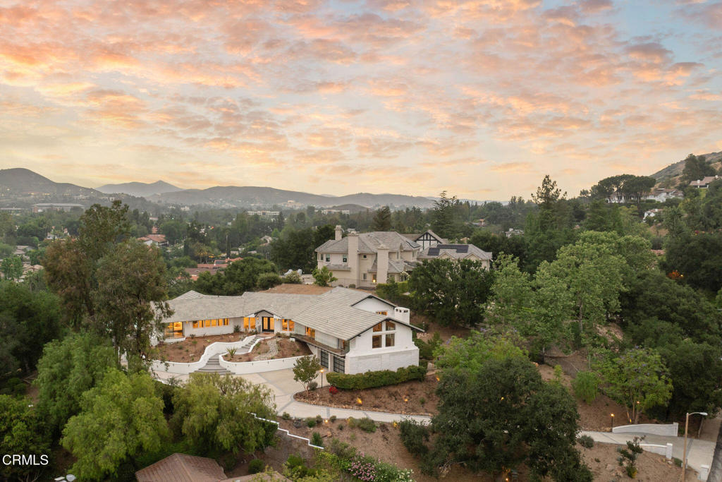 Perched well above street level and set behind a long driveway, this custom home has been refined with contemporary styling and offers unforgettable views and extreme privacy in idyllic Westlake Trails. A grand double-door entry opens to large, bright living spaces with wood floors, high-beam ceilings and an abundance of oversized windows flooding the home with tons of natural light and showcasing spectacular views throughout. The step-down living room offers views, a sleek fire feature and an adjacent wet-bar with Carrera marble and counter seating. The gorgeous kitchen is generously equipped with glass-front shaker cabinetry, Carrara marble counters and backsplash, a large island and high-end appliances including a built-in wine fridge and espresso machine. The open layout flows into a family room with a beautiful floor-to-ceiling tiled fireplace, more oversized windows and balcony access connecting a beautiful interior space with views of the Conejo Valley. This home offers two generously sized bedroom suites; one on the main level and one on the lower level, creating privacy and versatility for usage. In addition, a spacious loft with en-suite bath, walk-in closet and private balcony offers the flexibility to be used as a fabulous 4th bedroom suite, dedicated office space or other creative space. The sizable primary suite captures stunning views with a high wall of windows and a glass door accessing the pool, spa and outdoor lounging spaces. The high beam ceiling, modern chandelier and wooden feature wall add modern character to this sophisticated retreat. The en-suite bathroom is spacious and finished with dark stone, oversized shower, floating dual vanity, separate water closet, walk-in closet and more incredible views. Outside, the panoramic Conejo Valley views are a show-stopper in the rear yard. Relax and lounge on the patio, one of the multiple balconies or in the pool/spa surrounded by breathtaking views. Out front, a three-car garage and massive, long driveway provide ample parking or extra play space. A majestic oak tree is a perfect complement to the property, offering shade and a touch of whimsy with swings swaying gently beneath huge, twisting branches. Sweeping panoramic views, exceptional privacy and freshly redesigned with contemporary styling, this incredible custom home is a private haven perfectly situated in one of the most sought-after neighborhoods of Westlake Village.