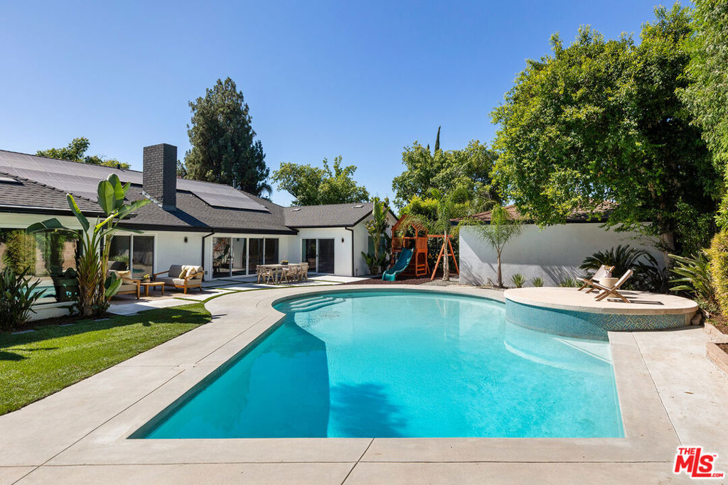 Stunning Mid-Century Charles DuBois Architectural with Pool in Prime Woodland Hills. Located on a desirable corner lot in one of the most sought-after areas of Woodland Hills, this impeccably remodeled Mid-Century Charles DuBois home offers over 3,000 sq ft of thoughtfully designed living space with 4 bedrooms and 3.5 bathrooms. Step through a custom oversized front door into a sun-drenched, open-concept interior featuring soaring ceilings with exposed beams, wide-plank white oak floors, and a dramatic Venetian plaster double-sided fireplace separating the formal living and dining areas. The chef's kitchen is a showpiece designed for both entertaining and everyday living. Highlights include a striking waterfall island, sleek wood and glossy white cabinetry, gold vein Calacatta countertops, and top-tier appliances including a panel-covered Fisher & Paykel fridge, Miele dishwasher, Frigidaire double oven, and Thor gas range. No detail was overlooked in this one-of-a-kind renovation: designer light fixtures, floating vanities, custom accent walls, solid extra-tall wood doors, and premium tile and finish selections throughout. The luxurious primary suite features cathedral ceilings with a central beam, a spa-like bath with a freestanding tub, floating double vanity, oversized walk-in shower, and a massive custom walk-in closet. Additional highlights include a spacious laundry room and pantry with smart controls, and a separate en-suite bedroom located on the opposite wing of the home ideal for guests or multigenerational living. Step outside to a private resort-like entertainer's backyard with newly designed hardscape, lush modern landscaping, and a large sparkling pool. Major upgrades include newer roof, dual HVAC systems, updated electrical panel, tankless water heater, recessed lighting, CAT wiring, plumbing, and all new pool equipment, plaster, tile, and coping. A detached garage with a private side entrance offers excellent ADU potential. Ideally located near top-rated charter schools, Bristol Farms, Calabasas Commons, Topanga Village, and the beloved local Farmer's Market, with quick access to the 101 freeway.