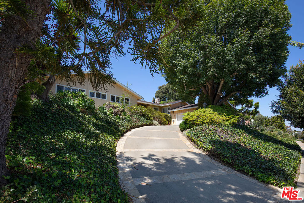 Tucked into the heart of the Huntington Palisades, this 1956 single-level Mid-Century home captures ocean views from its elevated 13,315 sq.ft. lot. A tree-lined driveway introduces the home, which opens into expansive light-filled interiors where vaulted wood-beamed ceilings and wide-plank oak floors set a warm, natural tone. Walls of sliding glass frame views of lush gardens and invite seamless indoor-outdoor living. The four-bedroom, three-bath layout includes generous living areas, one anchored by a sculptural stone fireplace and a galley-style kitchen that retains its original charm with a signature brick hearth, granite countertops, and custom cabinetry. The spacious primary suite boasts direct access to the terrace, a dedicated dressing room with a built-in vanity, and a bathroom featuring dual sinks, a soaking tub, and separate shower. Glass doors open to a private backyard sanctuary, where a pool is surrounded by mature landscaping and stone patios, offering privacy and tranquility in one of the Westside's most sought-after neighborhoods.