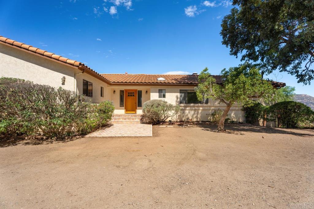 Welcome to this expansive and thoughtfully designed estate, offering comfort, functionality, and true country living with modern conveniences. Nestled in the back of the San Diego Country Estates, this property provides peace and privacy while still being close to community amenities, schools, and freeway access. Step inside to soaring ceilings and a spacious living room anchored by a wood-burning stove with gas start. The open layout flows seamlessly to a large family/dining room area, an open kitchen with large pantry area, and a private office with elegant acacia floors and a half bath. The primary suite is a true retreat, featuring two large closets with built-in organizers, real wood floors, and a luxurious bath with double sinks, walk-in shower, and soaking tub. A private slider leads you to the backyard oasis with hot tub and wraparound deck to enjoy the sweeping views. Two additional guest bedrooms with large closets share a full bath with dual sinks and separate shower/tub area. A spacious laundry room offers abundant storage, cabinetry, and a gas dryer connection. Energy efficiency and convenience are built in with central heat and zoned A/C (three zones), whole-house fan, EV charging station, whole-house RO and soft water system, and 48 paid solar panels with inverters in the garage. The three-car garage also provides ample space, while the basement includes a semi-finished bonus room in addition to a large air-conditioned area that can be finished for additional living space, wine cellar, craft room, etc. Outdoors, the property is a true homesteader’s dream with abundant fruit trees including citrus, peach, nectarine, apple, macadamia, blood orange, and grapefruit. The grounds feature a 12-station irrigation system, two outbuildings, a walk-in henhouse, corrals, a horse wash rack with power and water, and a tack room with electricity. Gardeners will love the automatic-timed garden irrigation. Additional upgrades include a 350-gallon propane tank, and a newer 10,000-gallon water tank with liner and pressure pump. With an electric gate to the garage, wraparound deck for entertaining, and plenty of space to live, work, and play, this property offers the best of rural living with modern luxuries.