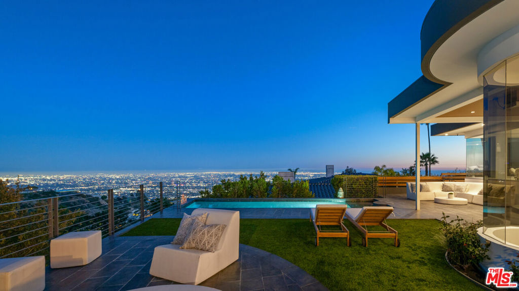 Perched atop the coveted Bird Streets in Doheny Estates, 9353 Nightingale Drive is an architectural triumph that seamlessly blends modern luxury with breathtaking panoramic views. This exquisite residence boasts an open-concept design, where soaring ceilings, floor-to-ceiling glass walls, and expansive living spaces create an effortless flow between indoor and outdoor living. The sleek chef's kitchen is a culinary dream, featuring top-of-the-line appliances, custom cabinetry, and a stylish islandperfect for both entertaining and everyday living. Just beyond, an outdoor BBQ and seating area provide the ideal setting for al fresco dining. The primary suite is a private sanctuary, offering head-on city views, a cozy fireplace, a serene seating area, and a spa-inspired bath. A dream walk-in closet, designed with double functionality as a panic room, adds a touch of discreet sophistication. For ultimate entertainment, the home has a dedicated media room, a fitness area, and a full bar with seating, accompanied by a temperature-controlled wine cellar. The resort-style backyard is an oasis of relaxation, complete with a stunning pool, fire pit, and multiple outdoor lounge spaces all set against the dazzling backdrop of Los Angeles' skyline. Other features include an elevator, a fireproof room, a state-of-the-art security system, and a two-car garage equipped with lifts to accommodate additional vehicles. Just moments from the world-class dining, shopping, and entertainment of the Sunset Strip, this extraordinary residence presents a rare opportunity to own one of the most iconic homes in Los Angeles.