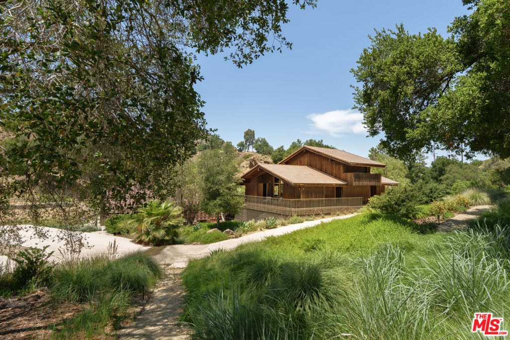 A Zen-Inspired Architectural Retreat in the Heart of Malibu. Discover one of Malibu's most distinctive architectural gems - an Asian-influenced, post-and-beam redwood and walnut sanctuary set on 10 private acres of rolling hills. This custom-designed retreat offers a truly tranquil lifestyle, where panoramic mountain views and a profound connection to nature create a serene, creative haven. The great room features soaring beamed ceilings and expansive windows that flood the home with natural light and frame the majestic landscape. The open kitchen offers Miele appliances while the primary suite is a private sanctuary with sweeping views and direct access to a large deck that wraps around the house, offering wide spaces for entertaining or lounging in the fresh air. Truly an ideal space to unwind, reflect, or ignite your next artistic endeavor, whether it be a screenplay, novel, album, or painting. A versatile loft adds flexibility as a studio, office, or additional sleeping area. Formerly restored by actor/director Vincent Gallo, the property exudes creativity and artistic energy. Outdoors, the grounds offer a graceful meditation ramada and matching pavilion bridge set over a seasonal stream; while meandering paths offer walks through your own canyon adorned with redwoods, oaks, seasonal waterfalls, and creeks. With zoning for light agriculture and equestrian use, there's room to expand, create, or cultivate. Ample parking makes entertaining and filming effortless, while proximity to Westlake Village, Malibu beaches, schools, shopping, lakes, golf, and tennis clubs ensures convenience without compromise. Owner has an expired permit for a 1,691sf art barn. Prop is not in Coastal Commission. Many possibilities abound.