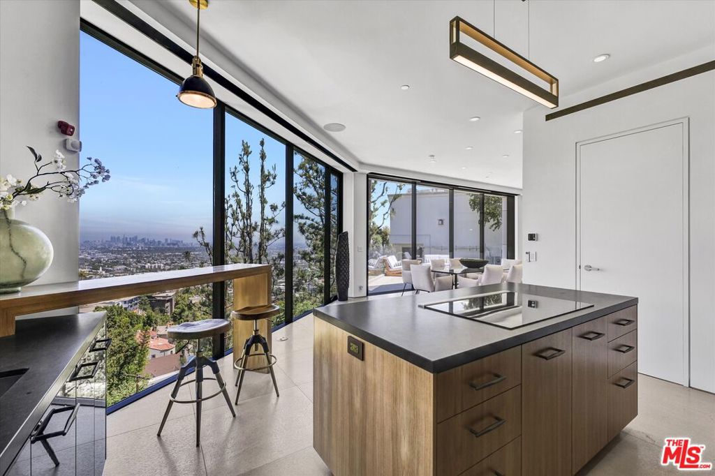 Welcome to modern luxury perched in the iconic Hollywood Hills! This newly completed contemporary masterpiece offers, featuring 4 bedrooms, 5 baths, and breathtaking panoramic views of Los Angeles and the Downtown skyline. Designed for seamless entertaining and everyday comfort, the home showcases a chef's kitchen equipped with top-of-the-line Wolf appliances, Italian tile accents, and sleek hardwood floors throughout. A stunning architectural waterfall cascades through the center of the home, creating a serene focal point and elevating the modern aesthetic. Enjoy an unparalleled entertainment experience with a dedicated media room, bar room, integrated surround sound system, and smart home technology controlling lighting, music, and climate. Luxurious spa-inspired baths include a steam shower for ultimate relaxation. Two expansive decks capture sweeping city views, while the exceptionally rare, flat 2,500 sq ft backyard provides valuable usable space perfect for outdoor entertaining, lounging, or the addition of a pool to complete your personal oasis. Additional highlights include a versatile guest house above the garage, ideal for visitors, extended family, or creative use. Parking includes a two-car garage plus a carport for added convenience. Perfectly located north of the Sunset Strip and moments from the vibrant energy of the Comedy Store, world-class dining, nightlife, and Runyon Canyon hiking trails, this Hollywood gem delivers the quintessential LA lifestyle.
