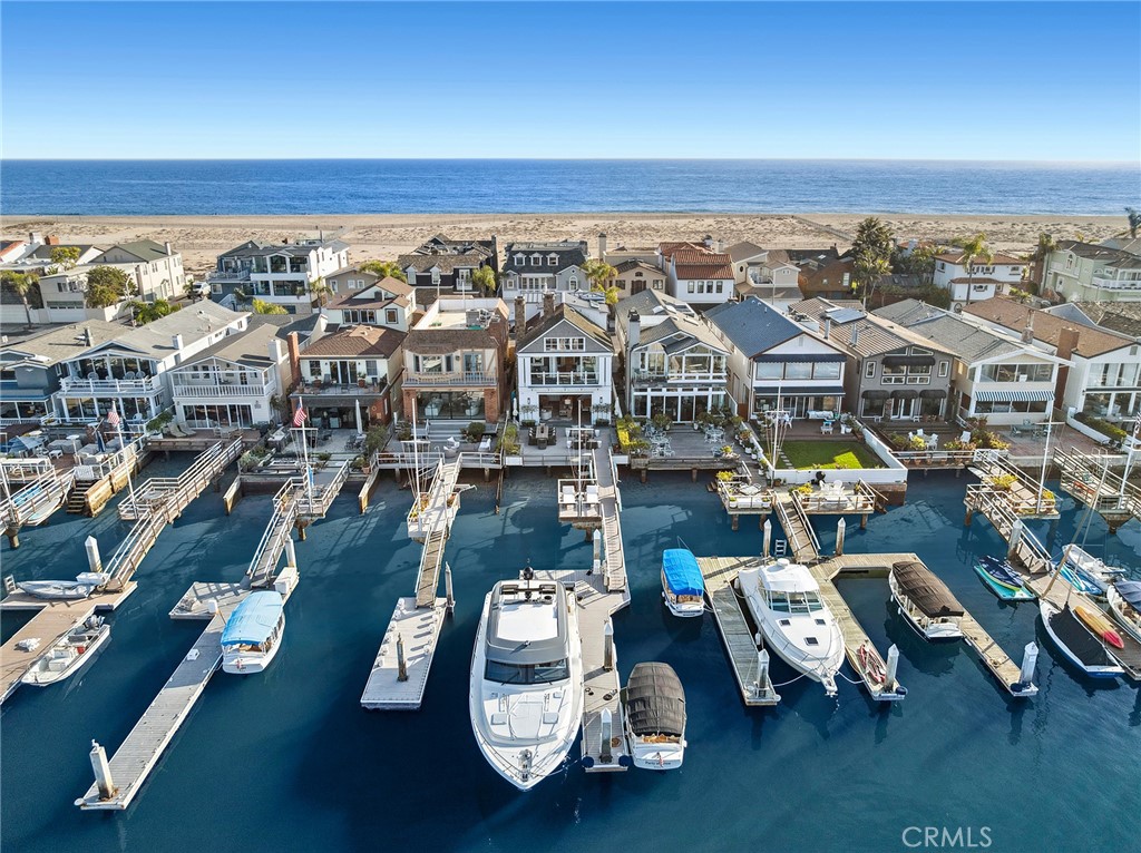 Experience timeless coastal elegance in this striking Cape Cod-inspired bayfront home, where panoramic water views and classic architectural charm create the ultimate waterfront escape. Conceived by noted Brandon Architects and crafted by premier homebuilder, Spinnaker Development, this turn-key waterfront residence features bespoke finishes at every turn. Step inside to discover sun-drenched living spaces adorned with shiplap walls, wide-plank hardwood floors, and crisp white finishes that echo the timeless elegance of New England’s coastal homes. The open-concept floor plan flows effortlessly from the professional-grade kitchen with marble countertops, walk-in pantry, and custom cabinetry to the expansive great room anchored by a cozy fireplace, and walls of glass that frame views of the harbor and make indoor-outdoor living and entertaining a breeze. Wake up each morning to stunning sunrises over the water from the impressive primary suite, highlighted by vaulted ceilings, a private balcony, and spa inspired ensuite bath with adjoining walk-in dressing area. Two additional ensuite bedrooms are well-appointed and offer comfort and privacy for guests or family. With an elevator servicing all three levels of the home the versatile rooftop loft with adjoining full bath offers a stylish, light-filled space perfect for a home office, media room or extra sleeping area. Step outside onto the roof deck, where the spa awaits—an ideal spot to unwind under the stars, and soak in the sea breezes. Designed to embrace the best of coastal living the home was conceived for a seamless connection between interior and exterior living. Dine al fresco on the bay front terrace, or gather around the firepit as the sun sets, casting a warm glow on the water – a perfect setting for evening cocktails. Enjoy boating, paddle boarding, or simply the tranquility of the bay from your private dock. A home that delivers the ultimate coastal lifestyle opportunity.