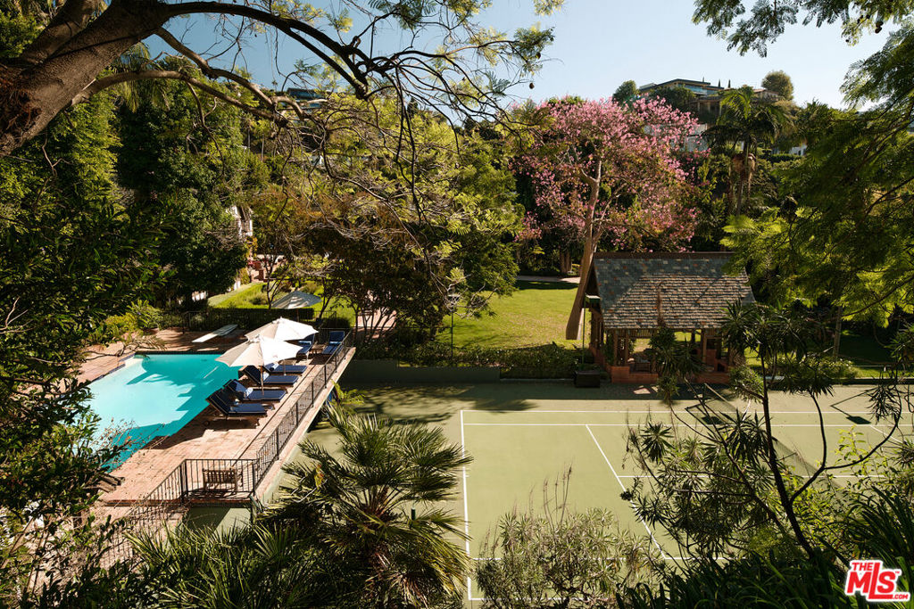 For the first time in over half a century, this majestic tennis court estate avails itself. In 1927 this specific site was built to become the largest and most private compound in all of the 'Bird Streets'. Situated on just under two verdant acres and set behind a discreet gated driveway, this blend of architecture, landscape, and rolling lawns is a complete juxtaposition to living in the heartbeat of the city. The centerpiece of this distinctive compound is this approximate 5,800 sq foot main home consisting of five bedrooms and six bathrooms. Steeped in authentic characteristics of a Tudor home, the exterior has an earth-toned color palette, leaded quarrel glass windows, large brick wood burning fireplaces, and timeless slate roofing. The authenticity dramatically carries into the interior with timbered ceilings, arched doorways, dark wood paneling, and a wooden staircase. Once inside, one is immediately drawn to the step-down living room with the original wood burning fireplace that seamlessly leads to a light bright sunroom and a bespoke bar transported from London. The first floor also consists of a generous eat-in kitchen, formal dining room overlooking the front garden and a warm window-wrapped den with a paneled conservatory-style ceiling. Upstairs, the vast primary suite has a large private balcony overlooking the koi pond with the sounds of a gentle waterfall. There are period-rich wood-panelled duel bathrooms, and large dressing rooms, both with private-office features and built-in cabinets indicative of the era, both with garden views through oriel windows. Two further bedrooms with ensuites, and window seats round out the second floor. The romantic A-framed peaked the third floor features a tree-top level bedroom, bathroom, and gym. The grounds designed by Mark Rios epitomize an English estate with gravel driveways, brick pathed vignette entertainment spaces, a vast rolling lawn suitable for croquet, a stunning oval water lily pond with fountain, integrated outdoor kitchen, and dining space with a grand wood burning fireplace. Mature towering trees provide not just privacy but ample sound barriers from the city below, rock pools, koi ponds and waterfalls abound. Rose, fruit and kitchen gardens lead off the house, while multiple meandering paths, one of which leads to a private sitting area that overlooks the grounds called the 'Bird Nest' provide a unique tranquil setting. Further amenities include a north/south championship tennis court with viewing pavilion, an elegantly fenced swimming pool with a well-appointed vaulted pool house. A two-story carriage house/garage with a double-height guest suite and library wall and vast wine cellar, suitable for any serious collector. This storied property has been home to very few, but its guests have been a venerable who's who of entertainment moguls, movie stars, rock royalty and Angeleno elites. A truly beautifully maintained piece of property with unmatched provenance.
