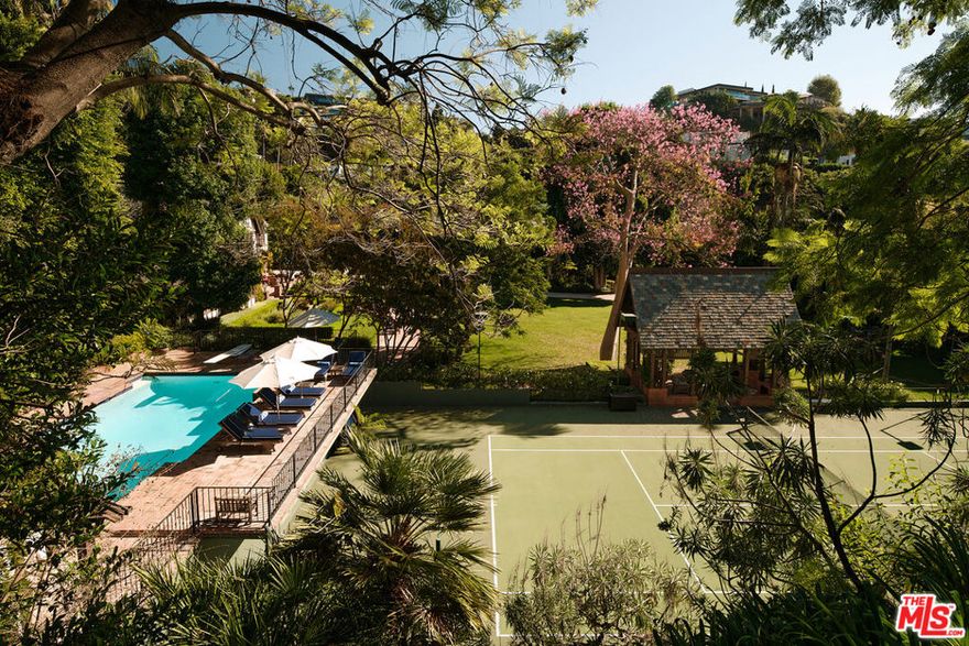 For the first time in over half a century, this majestic tennis court estate avails itself. In 1927 this specific site was built to become the largest and most private compound in all of the 'Bird Streets'. Situated on just under two verdant acres and set behind a discreet gated driveway, this blend of architecture, landscape, and rolling lawns is a complete juxtaposition to living in the heartbeat of the city. The centerpiece of this distinctive compound is this approximate 5,800 sq foot main home consisting of five bedrooms and six bathrooms. Steeped in authentic characteristics of a Tudor home, the exterior has an earth-toned color palette, leaded quarrel glass windows, large brick wood burning fireplaces, and timeless slate roofing. The authenticity dramatically carries into the interior with timbered ceilings, arched doorways, dark wood paneling, and a wooden staircase. Once inside, one is immediately drawn to the step-down living room with the original wood burning fireplace that seamlessly leads to a light bright sunroom and a bespoke bar transported from London. The first floor also consists of a generous eat-in kitchen, formal dining room overlooking the front garden and a warm window-wrapped den with a paneled conservatory-style ceiling. Upstairs, the vast primary suite has a large private balcony overlooking the koi pond with the sounds of a gentle waterfall. There are period-rich wood-panelled duel bathrooms, and large dressing rooms, both with private-office features and built-in cabinets indicative of the era, both with garden views through oriel windows. Two further bedrooms with ensuites, and window seats round out the second floor. The romantic A-framed peaked the third floor features a tree-top level bedroom, bathroom, and gym. The grounds designed by Mark Rios epitomize an English estate with gravel driveways, brick pathed vignette entertainment spaces, a vast rolling lawn suitable for croquet, a stunning oval water lily pond with fountain, integrated outdoor kitchen, and dining space with a grand wood burning fireplace. Mature towering trees provide not just privacy but ample sound barriers from the city below, rock pools, koi ponds and waterfalls abound. Rose, fruit and kitchen gardens lead off the house, while multiple meandering paths, one of which leads to a private sitting area that overlooks the grounds called the 'Bird Nest' provide a unique tranquil setting. Further amenities include a north/south championship tennis court with viewing pavilion, an elegantly fenced swimming pool with a well-appointed vaulted pool house. A two-story carriage house/garage with a double-height guest suite and library wall and vast wine cellar, suitable for any serious collector. This storied property has been home to very few, but its guests have been a venerable who's who of entertainment moguls, movie stars, rock royalty and Angeleno elites. A truly beautifully maintained piece of property with unmatched provenance.