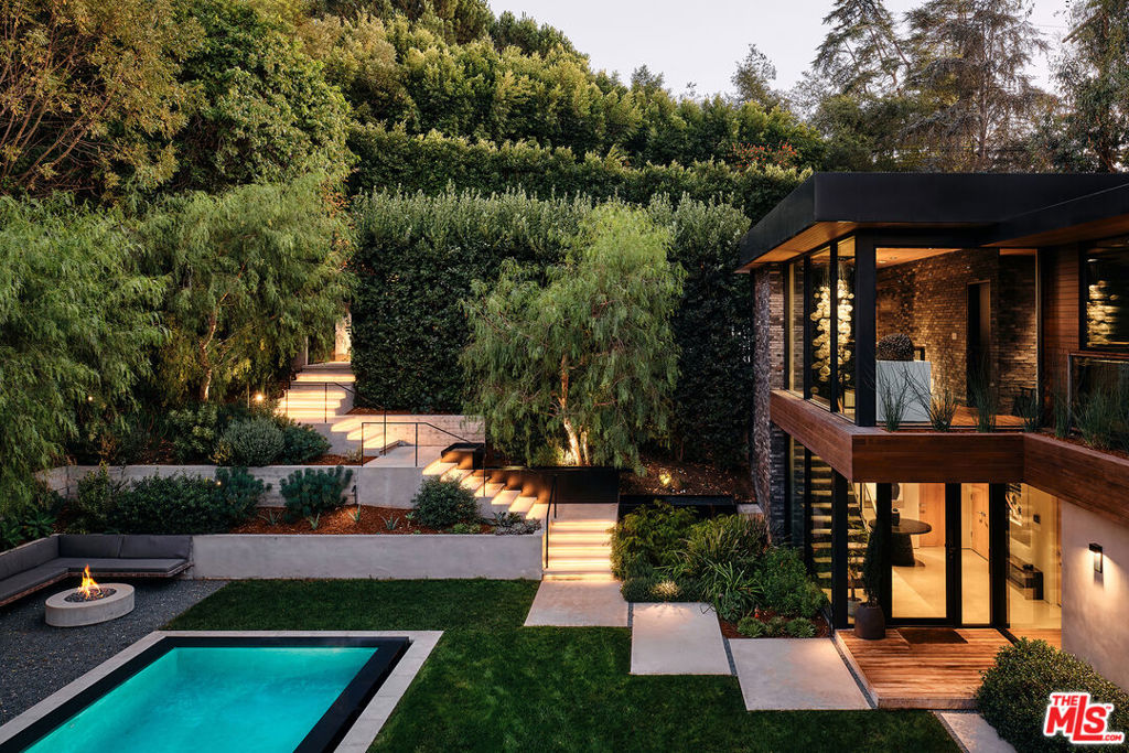 Nestled within the prestigious gated enclave of Oak Pass Road in Beverly Hills, this 5,442-square-foot modern sanctuary embodies a rare synergy of architecture and nature. Positioned on a peaceful .32-acre lot, this 3-bedroom, 5-bathroom retreat offers a secluded haven with panoramic canyon and hillside vistas. Thoughtfully crafted with wood, stone, glass, and fire elements, each room welcomes the outdoors through expansive floor-to-ceiling glass, creating a zen-inspired atmosphere for ultimate relaxation.The home's L-shaped design and sculpted landscape enhance privacy, embracing the surrounding natural beauty. A dramatic two-story atrium fills the space with light and greenery, complemented by floating fire features and suspended gardens that deepen the sense of calm. Flowing seamlessly from the formal dining room, the open living area connects to an expansive kitchen with dual sided fireplace, that opens to the outdoor covered lounge area for effortless entertaining. The primary suite appears to float above a saltwater infinity pool, offering breathtaking views, while two guest suites rest under the canopy of a majestic 100-year-old oak tree.Terraces along the property reveal sweeping views of the private backyard and surrounding mountains, with an inviting spa and lounge area designed for alfresco dining and gatherings. A dedicated gym and wellness area, private studio/office, theater room, and an outdoor kitchen with a fire pit complete this residence, a true celebration of refined, tranquil living in an extraordinary setting.Oak Pass Road is an exclusive gated neighborhood in Beverly Hills Post Office situated west of North Beverly Park, with only 42 private residences offering unparalleled access to the shopping, dining and nightlife of Rodeo Drive and the iconic Beverly Hills Hotel. Simo Designs.