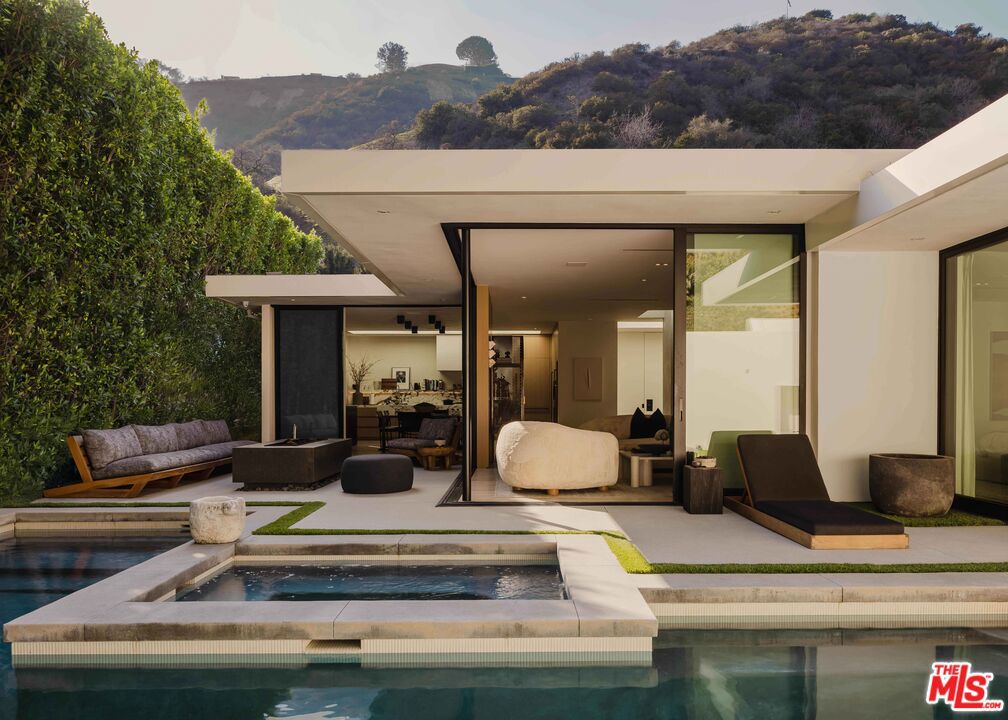 Tucked away just north of Sunset and the iconic Beverly Hills Hotel, 1952 North Beverly Drive is a sleek, single-story residence that balances refined international design with effortless California living. Designed by Yoram LePair (a Gehry Partners alum) and illuminated to perfection by noted lighting designer Mark Raissen (Sunset Tower Bar, San Vicente Bungalows), the home is defined by refined silhouettes, an abundance of natural light, and fluid indooroutdoor connection. Expanses of floor-to-ceiling glass, meticulously detailed rift-oak paneling, and wide French oak planks in generous proportions set a sophisticated tone. The kitchen is conceived for openness and connection, inviting conversation and versatile entertaining with a large, centralized dining area as a natural gathering space for shared meals. Appliances include premier selections from Sub-Zero, Wolf, and Miele, along with wine refrigeration for 300 bottles and a full-service wet bar detailed in blackened steel, ebony millwork, and honed Saint Laurent marble. A formal living space orients toward the yard and pool, capturing views of the softly rising hillside that extend toward the gated entrance of Franklin Canyon Park. The primary suite offers an expansive walk-in wardrobe with thoughtfully designed dressing areas, and a luxurious bath finished in stone and tailored millwork, with sleek pocket doors that blur thresholds with graceful simplicity. A secondary bedroompresently configured as a denserves as a retreat for entertainment and quiet conversation, with a discreetly integrated full bath concealed behind sculpted oak walls. Outdoors evoke the atmosphere of a boutique hotel, with a firepit lounge framed by teak sofas, a pool and spa detailed in muted Japanese tile, and a large fireplace thoughtfully incorporated into a bespoke garden wall. Multiple SONANCE speaker systems complete the setting, creating a fully immersive environment for an activated outdoor lifestyle. Intelligent living is defined by Control4, Lutron, and AI-driven automation. The detached guest casita (fully permitted with its own address at 1954 North Beverly) offers the ultimate in private accommodation, with a stone-clad bathroom, custom wardrobe, concealed refrigeration, and dedicated storage. A separate laundry/tech room includes additional wine refrigeration and generous organizational space. The restrained exterior faade blends discretion and design, softened by native landscape architecture from Elysian Landscapes. Covered parking is secured behind an 8-foot louvered steel gate, maintaining the residence's understated presence.