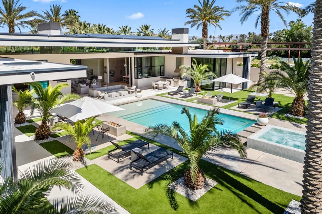 A rare opportunity to own one of the Coachella Valley's most magnificent contemporary estates, this architectural masterpiece embodies modern desert luxury. Set on a private half-acre within an exclusive enclave of ten custom residences, this gated retreat offers the ultimate in privacy and sophistication. Beyond the striking entry, mountain vistas take your breath away and stately palms frame the home's elegant design. The 80-foot-long great room with soaring 16-foot ceilings seamlessly blends formal and informal living, while a 30-foot motorized Fleetwood pocket door vanishes, unveiling a stunning outdoor oasis with a pool, spa, and multiple seating areas for a true indoor-outdoor experience. The gourmet kitchen, outfitted with premium Gaggenau appliances, flows effortlessly into the living and dining areas. The primary suite is a private sanctuary with a fireplace, lounge area, spa-inspired bath, and a custom boutique-style closet. The opposite wing offers three en-suite guest rooms, while a detached guest house with a bedroom, bath, living area, kitchenette, and intimate patio provides the perfect retreat for guests. Additional features include an owned solar system, whole-home water filtration, Sonos, Vantage smart home automation, motorized window treatments, and honed limestone floors throughout. Just minutes from Clancy Lane, El Paseo, and Coachella Valley's world-class golf, tennis and renowned amenities, this home is a statement of unparalleled style and refinement.
