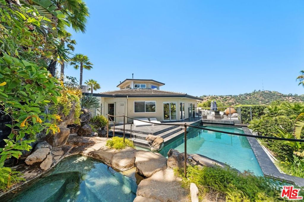 RESORT-STYLE HIDEAWAY WITH BREATHTAKING VIEWS IN THE HOLLYWOOD HILLS. As you arrive at the end of a private road, a sense of tranquility sets in. The gates open to reveal a secluded contemporary estate perched atop a majestic hilltop promontory. Step inside, and you're immediately drawn to the sweeping canyon views that instantly make you feel above it all. Polished stone floors guide you through the expansive open layout, where nearly 3,000 square feet of curated luxury unfolds. The sleek, modern kitchen opens to a living space where light filters in through massive sliding glass doors, blending indoors and out with ease. Step through them, and you're on one of several private terraces, the gentle sound of cascading water in the distance beckoning you further. Each of the three spacious bedrooms is a private retreat, complete with its own ensuite bath. The loft offers a serene space to read, work, or simply take in the vistas. A discreet safe room adds peace of mind, while the upscale finishes throughout reflect careful attention to detail. Outside, the magic continues. You're enveloped by lush landscaping and multiple lounge areas that feel like private cabanas. The centerpiece? A dramatic infinity-edge lagoon-style pool with a two-story waterfall and inviting spa. Whether you're entertaining under the stars or enjoying a quiet morning swim, every corner of this property invites peace, pleasure, and indulgence. This isn't just a home, it's a sanctuary above the city. Don't miss your chance to experience true resort living in the Hollywood Hills. Lease available fully furnished.