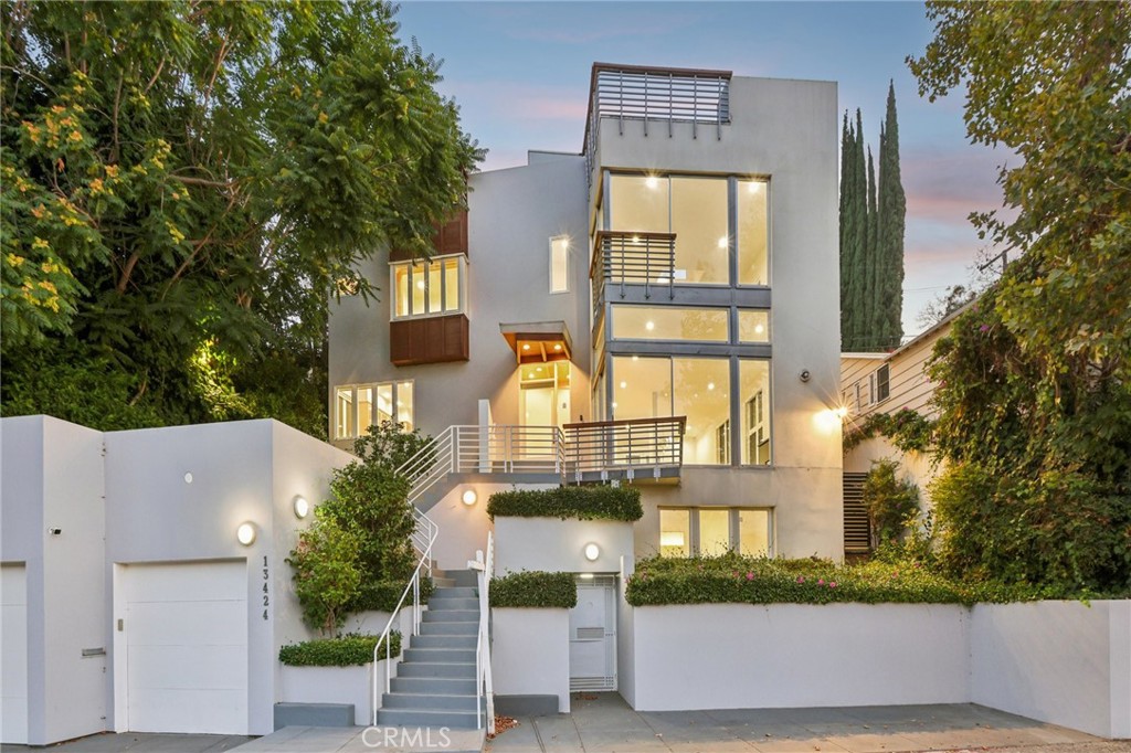 Welcome to this contemporary hideaway nestled south of Ventura Boulevard on a picturesque, tree-lined street in coveted Sherman Oaks. A striking architectural facade with geometric glass panels sets the stage for the light-filled interior, where floor-to-ceiling windows bathe the formal living and dining areas in California light, highlighted by an onyx fireplace and custom built-ins. The open-plan kitchen features stainless-steel appliances, abundant cabinetry, and a central island with a cooktop, flowing effortlessly into the family room, which opens via French doors to outdoor entertaining spaces. A private elevator connects all levels, leading to a generous rooftop deck with sweeping 360-degree views of the Valley, city lights, mountains, and treetops. The voluminous primary suite includes its own fireplace, Juliet balcony, spa-inspired bath, and walk-in closet. Secondary bedrooms are bright and spacious, and one has been thoughtfully appointed as a gym with mirrored walls and rubber flooring. Moments from Ventura Boulevard’s shops and dining, and located within the top-rated Dixie Canyon Community Charter district, this home embodies sophisticated hillside living with convenience and style.