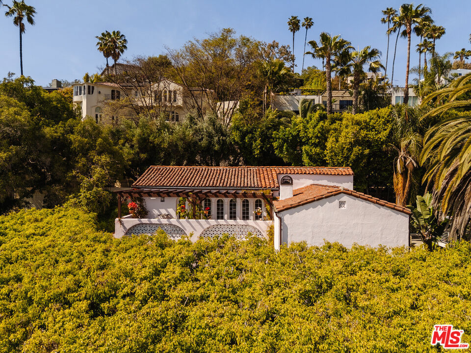 Located in the heart of Los Feliz and adjacent to Laughlin Park, this gated and private 3BR/3BA Spanish home circa 1924 blends original romantic Spanish details with modern updates. Soaring beamed ceilings with iconic hand-painted murals, vibrant colors, and abundant charm are found at every turn. The home offers a flexible downstairs layout with a spacious family room, formal dining room, updated contemporary kitchen and guest bedroom with bath. Upstairs is a balcony library leading to a second bedroom and bathroom, as well as the primary suite with custom millwork wardrobe and gorgeous en-suite bath with steam shower. A series of arched French doors open to a private balcony patio with sweeping views of Downtown Los Angeles and beyond, framed by jasmine and palm trees. A tiled patio and lushly landscaped garden offer a private escape, featuring a petanque court and multiple areas for dining and entertaining. Located just minutes from Griffith Park, Hollywood, and Los Feliz Village, come discover this true work of art in one of the city's most desirable neighborhoods.