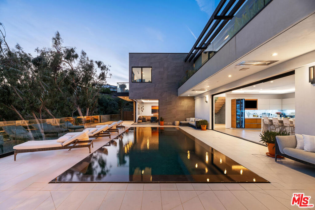 Perched atop a coveted, gated promontory in the hills of Brentwood, this striking architectural estate offers an extraordinary blend of cutting-edge design, luxurious scale, and ultimate privacy in one of the Westside's most prestigious enclaves. Set behind a long, gated driveway and commanding an impressive 200 feet of unobstructed frontage, the nearly 10,000-square-foot residence captures sweeping, wraparound views from downtown Los Angeles to the Pacific Ocean and Catalina Island beyond. Designed for both grand-scale entertaining and elevated daily living, the home's gallery-style interiors feature soaring ceilings, minimalist lines, and expansive walls, ideal for showcasing a significant art collection. Automated sliding glass doors create seamless indoor-outdoor living, opening to over 5,000 square feet of terraces and resort-like amenities. The breathtaking backyard features a zero-edge pool and spa, black marble bar, outdoor pavilion with built-in BBQ, and a large, flat grassy side yard perfect for kids, pets, or gardening, framed by manicured landscaping and unobstructed vistas. The estate includes six ensuite bedrooms and nine bathrooms, highlighted by a show stopping primary suite with panoramic views, a spa-inspired bath, and a boutique-style walk-in closet. Additional features include upper and lower-level lounges, a state-of-the-art screening room, temperature-controlled walk-in wine cellar, indoor-outdoor gym, family office, and Lutron home automation throughout. With exceptional design, privacy, and scale, this Brentwood estate represents a rare opportunity to own a truly world-class residence in a premier Los Angeles location.