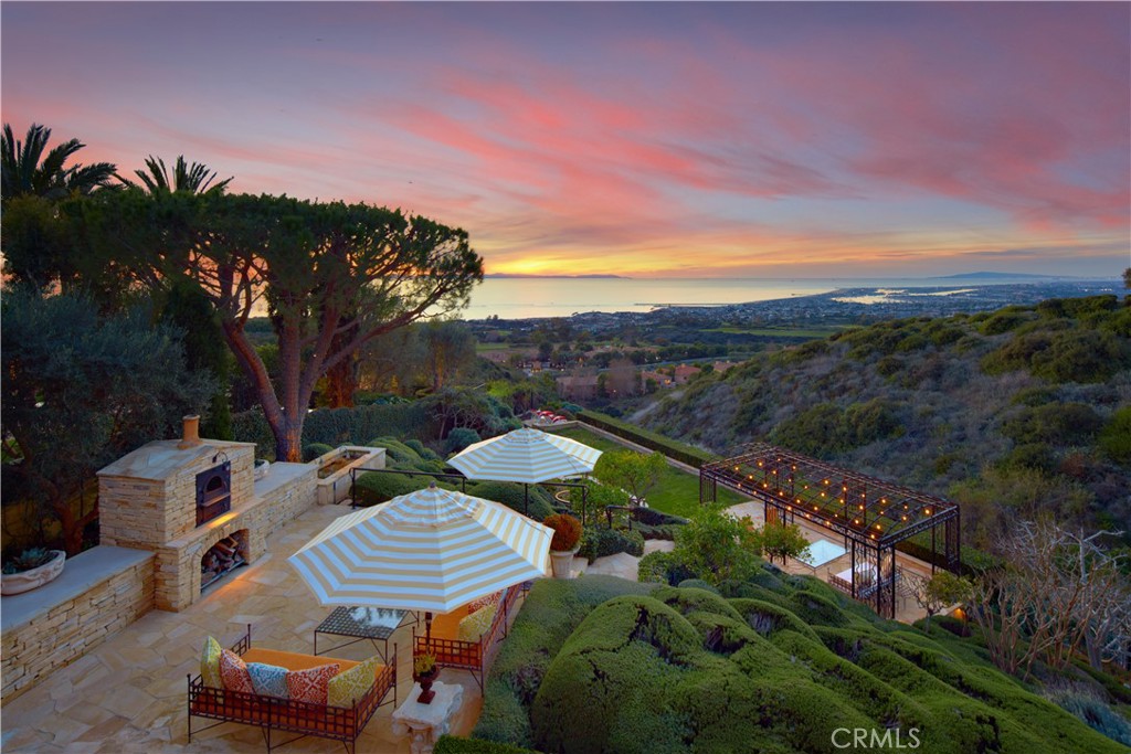 Ever-changing by day and night, the phenomenal panoramic views of 'Villa Saffron' are in a league of their own. They are experienced from both levels of the St. Tropez-inspired villa at guard-gated Pelican Crest in Newport Coast. The immersive vistas stretch across lush fairways, a canyon, the azure waters of the Pacific Ocean, Newport Harbor, San Clemente and Santa Catalina Island. Enchanting city lights reach as far as Palos Verdes. The terraced grounds tower 604 feet above sea level. They command front-row views that complement a backyard with upper and lower terraces, four lawn areas, loggias, custom fireplace/wood-burning pizza oven. The outdoor kitchen features a built-in 48" Lynx BBQ. Located close to the end of a private cul-de-sac, the villa showcases exquisite landscaping, a walled and gated front yard with a limestone colonnade pool, and a large, fireplace-warmed atrium. Spanning nearly 26,092 SF, the estate’s sumptuous homesite by EBTA architects, built by PrideMark, compliments an opulent interior that extends approximately 8,176 SF. It features four en suite bedrooms (one at entry-- currently used as an office), four full baths, and two half baths. An inviting foyer and grand staircase provides an elegant introduction to living areas including a media room, sunny office with enchanting views, a circular formal dining room surrounded by columns, and a spacious great room with an ornate hand-carved limestone fireplace. The chef’s kitchen boasts an oversized island, ocean-view breakfast room, butler’s pantry, two sinks, stone countertops, custom cabinetry, built-in side by side Sub-Zero refrigerator/freezer, steam oven, six-burner Wolf range, and double ovens. Note worthy materials include stone imported from France and Italy, antique French pavers, French white oak flooring, along with custom-made steel windows and French doors. All rooms except the media room offer access to an outdoor patio, terrace, loggia, or Juliet balcony, with the ocean-view primary suite boasting two decks, pocket doors at its entrance, a sitting room, two walk-in closets with custom built-ins, retractable sun shade, and luxe bath featuring a soaking tub and separate shower. Additional highlights include a 350+ bottle temperature-controlled wine cellar, wet bar, EV charging, full house water filtration and soft water by Water Techniques, Sonos sound system, Lutron lighting, as well as the option to build an ADU on the terraced lot with a spectacular view.
