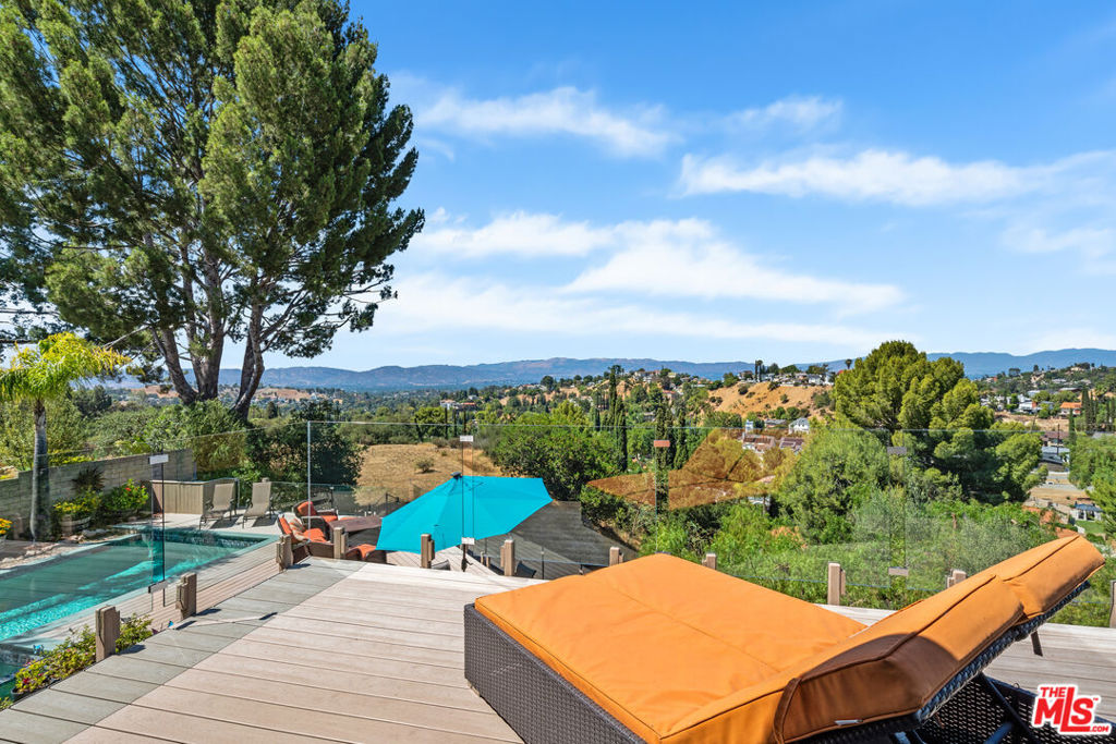 Just as this family did 25 years ago, you too will fall in love with the spectacular view from this exceptional home in Woodland Crest a hidden gem nestled within the serene Santa Monica Mountains. The charming covered porch and beautifully landscaped dry creek enhance the curb appeal of this elegant Spanish-style residence. Step through the double-door entry and be instantly drawn to the a wall of glass that frames an unforgettable view, effortlessly blending indoor comfort with natural beauty. Designed for both intimate gatherings and grand celebrations, this home has been the setting for countless cherished memories. The renovated chef's kitchen is a true showpiece, featuring top-of-the-line Jenn-Air appliances, including a 6-burner range with griddle, beverage refrigerator, custom cabinetry, Quartzite countertops with waterfall, a tumbled tile backsplash, a breakfast bar, and an additional dining area. The expansive family room offers custom built-ins and a dramatic stone fireplace with raised hearth perfect for cozy evenings. The primary suite is a private retreat with soaring vaulted ceilings, ample closet space, a beautifully updated bathroom with dual vanities, and a private balcony ideal for watching the sunrise and sunset. Two-story windows flood the home with natural light, creating an open and airy atmosphere throughout. Outside, the entertainer's backyard is a dream come true complete with a covered patio, sparkling pool, putting green, and citrus trees including lime and grapefruit. Host unforgettable gatherings on the massive Trex deck while taking in breathtaking city and mountain views. With the Los Angeles Rams' new training facility and the ambitious Warner Center 2035 Plan on the horizon, Woodland Hills is poised for exciting growth and transformation. Close proximity to Luxury shopping, the beach and exceptional schools makes this home not only a sanctuary but a smart investment in your future.
