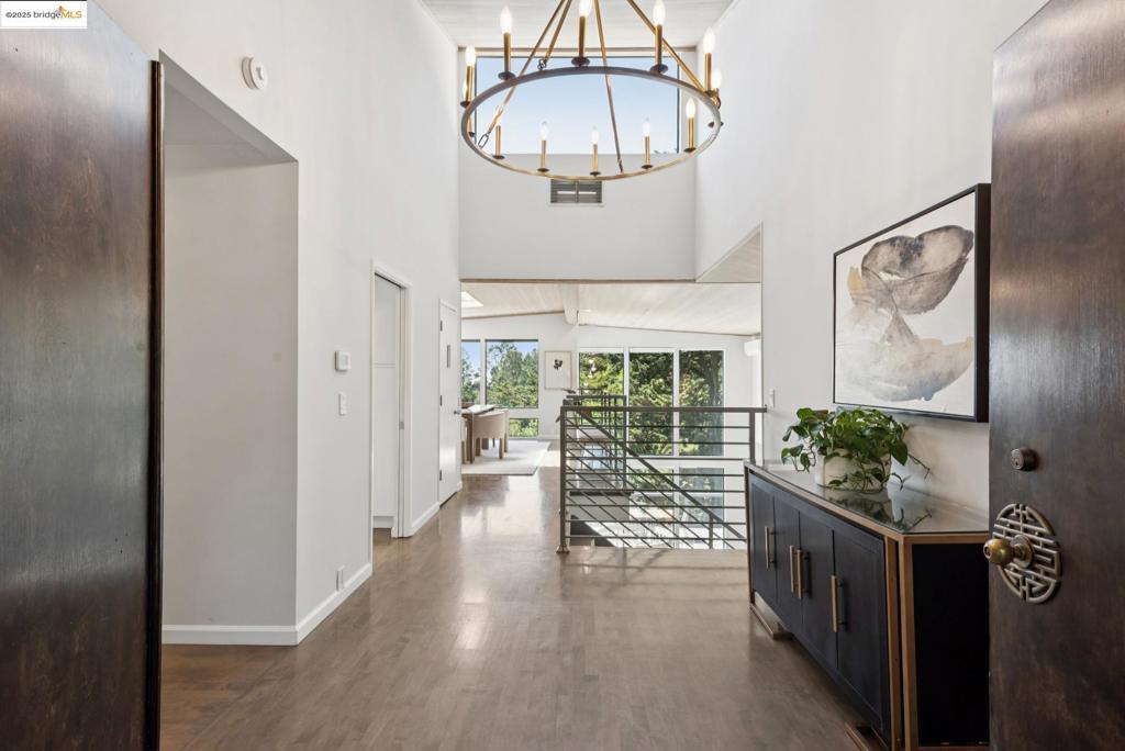 Tucked atop Ascot Drive on a serene side street, this custom contemporary residence blends striking architecture with natural beauty. Boasting 3,709 sq ft of light-filled living space, the home features soaring ceilings and dramatic floor-to-ceiling windows that frame captivating views of the Bay Bridge and glimpses of the Golden Gate. The airy entryway flows into a sleek, remodeled kitchen and adjoining dining area—perfect for entertaining against a breathtaking backdrop. The mid-level offers a spacious living room and two bedrooms, including a luxurious primary suite with its own fireplace, private patio access, a newly remodeled spa-like bath, and a large dressing room. The lower level provides flexible living with additional bedrooms, bathrooms, and separate entrances—ideal for an au pair, guests, or multigenerational living. Just minutes from Montclair Village and commuter routes, this tranquil retreat offers the best of modern living in a coveted hillside setting.