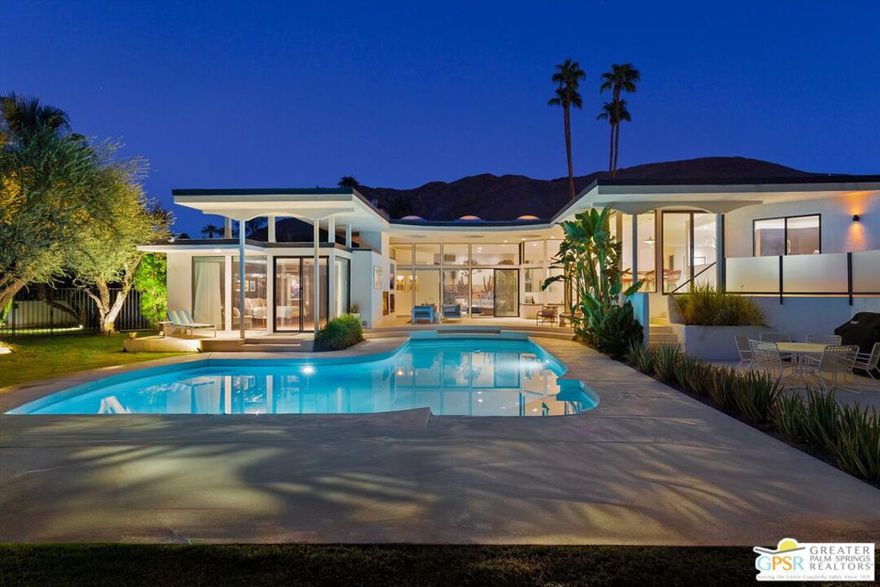Designed by renowned Hollywood set designer turned architect James McNaughton, this magnificent Mid-Century home embodies the drama and elegance of Palm Springs living with walls of glass showcasing panoramic views of Mt. San Jacinto, the Indian Canyons Golf Course, and the sparkling pool. A dramatic double-door entry opens to a light-filled great room with soaring arches, sunken living space, and seamless indoor-outdoor flow through multiple sliders. Luxurious finishes include Kenyan marble, honed limestone floors that extend outdoors, and striking circular skylights, complemented by three fireplaces and refined architectural details throughout. The gourmet kitchen is outfitted with concealed appliances, wine storage, and an ice maker, while the adjacent bar features a pass-through window to the poolside patio perfect for entertaining. Four ensuite bedrooms offer exceptional privacy, with the primary retreat boasting its own fireplace, coffee/wine bar, walk-in closet, and spa-like bath with dual water closets, soaking tub, and outdoor shower. Outdoor living is maximized with a covered lanai, fireplace, television, and breathtaking desert views with owned solar panels to ensure energy efficiency. Ideally located in South Palm Springs, this home is just steps from hiking, horseback riding, golf, and minutes from downtown.
