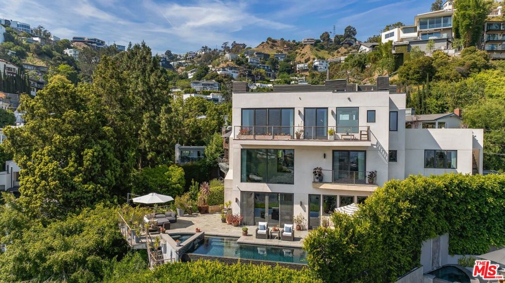Perched above the iconic Sunset Strip, this entertainer's paradise masterfully balances form and function with an open floor plan and seamless indoor-outdoor flow, ideal for California living. A grand entry leads to a dramatic double-height living room with soaring 30-foot ceilings and walls of glass that frame panoramic views while bathing the space in natural light. The professional-grade chef's kitchen is appointed with dual sinks, dual refrigerators, a separate breakfast area, soapstone countertops, and premium Wolf and Sub-Zero appliances. A formal dining room with French doors opens directly to the outdoors, creating an effortless transition for entertaining. Throughout, solid walnut flooring and lofty ceilings lend a sense of timeless sophistication.The oversized primary suite is filled with natural light and boasts its own fireplace, an expansive walk-in closet with skylight, and a spa-inspired bath with dual sinks, soaking tub, heated tile floors, and a dual shower with exquisite mosaic tile detail and a picture window perfectly capturing the city skyline. Three spacious guest bedrooms each feature en suite bathrooms, providing exceptional comfort and privacy for visitors.The lower level of this home provides an incredible escape with a large saloon appointed with a mahogany bar, a 14-seat movie theater and spacious gym. The rooftop deck and infinity pool seem to hover above Los Angeles, offering a truly breathtaking vantage point for unforgettable evenings.