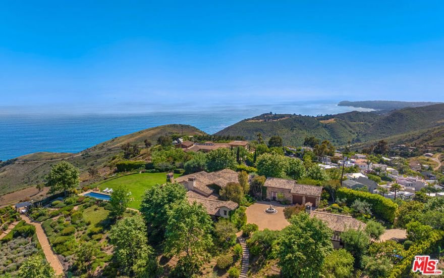 Tucked away behind gates atop the Malibu hills, this enchanting estate captures panoramic ocean and mountain views while evoking the timeless romance of a European countryside retreat. The approach unfolds along a long drive into a broad motor court with parking for 10+ cars, framed by lush gardens and anchored by a stone fountain.Inside, soaring wood-beamed ceilings, French doors, and gallery walls create a backdrop of warmth and elegance. The main living room is crowned by a monumental fireplace and flows to a formal dining room and chef's kitchen, where custom cabinetry, a walk-in pantry, dual ovens, a Viking range, Wolf six-burner cooktop, and a large stone-topped island cater to both intimate evenings and grand entertaining. Nearly every room opens to patios, gardens, or terraces, merging the indoors with the property's dramatic natural setting.The estate is designed with multiple wings for privacy. The primary suite features vaulted ceilings, a stone fireplace, and walls of glass that frame ocean and pool views. Its spa-inspired bath offers dual vanities, a soaking tub, and a large shower with multiple heads. Additional bedroom suites include private patios and marble-clad bathrooms, while a powder room delights with hand-painted lemon grove murals and a sculptural wood vanity. Beyond the main house, a detached office with vaulted ceilings, stone fireplace, reclaimed wood built-ins, and a wet bar creates the perfect studio or guest space. Across the court, a guest suite adjoins the garages, complete with wood floors, vaulted ceilings, en-suite bath, and French doors to a pergola-shaded patio. The outdoor living is extraordinary: a covered loggia with stone fireplace, alfresco dining, and heaters for year-round enjoyment; expansive lawns flowing to a long rectangular pool and spa with automatic cover; and terraced gardens with citrus groves, fountains, koi ponds, and box hedges. Meandering stone paths lead to a barn-inspired guest structure with a porch swing and firepit seating, all overlooking breathtaking ocean and canyon vistas. A professional-grade recording studio with soaring ceilings, custom acoustics, and a sound room enhances the estate's versatility, offering creative refuge for artists and visionaries. Throughout the property, hidden seating areas, romantic pergolas, and layered gardens create a sense of discovery and retreat. Exquisitely landscaped and thoughtfully designed, 2900 Corral Canyon Rd is a rare Malibu estate that combines European elegance, coastal serenity, and boundless possibilities for living, entertaining, and creating.