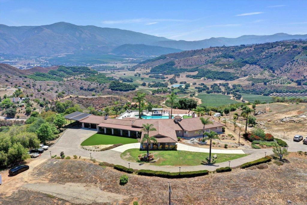 Exceptional Value! Experience a Lifestyle of Seclusion, Luxury, and Natural Beauty. Welcome to a truly extraordinary retreat nestled on over 8 acres in one of the most picturesque and private locations Southern California has to offer. Perched atop your own slice of mountain, this estate offers commanding, panoramic views that evolve with the seasons—cliffside horizons, rolling hills, and a peaceful valley stretching out below. Winding through the gated entrance, a private drive and stunning vistas set the tone for a lifestyle immersed in nature, yet remarkably convenient. Despite its seclusion, the property is just minutes from top-rated schools, wineries, beautiful golf courses, a private country club, and world-class casinos. You’re also just a short drive to Interstate 15, offering easy access to Temecula, San Diego, and beyond. The estate features a striking main residence estimated at 5,045 sq ft, complemented by a detached guest house of approximately 1,550 sq ft, rents for $2500 to current tenants, and a separate casita with private bath and kitchenette. Perfect for entertaining, multi-generational living, or a family compound, the layout offers both privacy and connection across beautifully appointed spaces. The guest house is currently rented to two older professional tenants on a flexible month-to-month lease, offering optional income potential without commitment—use it as-is, or reclaim the space for personal use. Outdoors, enjoy a fully lit basketball/pickleball/sports court, solar-heated pool and spa with sunken bar, cantilevered deck, putting green, gas fire pit, and resort-style lighting throughout the property. Inside, luxury meets practicality with dual HVAC systems, tankless water heaters, a whole-house generator (main house), security system with cameras and fire/CO2 detection, a 240V car charger, and an ethernet-connected smart entry system at the gate. Every element of the home is thoughtfully designed—multiple walk-in closets, spacious bathrooms, and generous garage capacity including a porte cochère, carport, and an additional pad ready for an RV garage or workshop. Whether you’re soaking in the spa beneath the stars, walking the trails, or enjoying a sunset from your deck, this is a rare sanctuary where peace, privacy, and beauty converge. Can transfer furnished