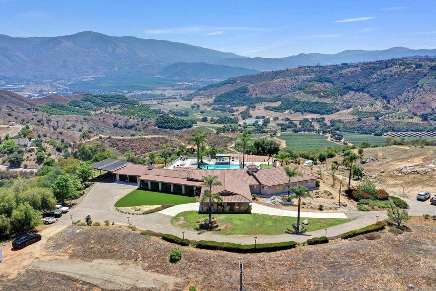 INTEREST RATES ARE DOWN—AND SO IS PRICE! Recent $10,000 reduction, this estate is now the best deal in Valley Center. Experience seclusion, luxury, natural beauty on over 8 private acres perched atop your own mountain with panoramic views of rolling hills, cliffsides, and valleys below. Property includes, Main Residence 5,045 sq ft of striking design and thoughtful layout. Guest House 1,550 sq ft, currently rented at $2,500/month to a professional, well-established couple on a month-to-month lease. They’re quiet, out of sight halfway down the hill, and willing to vacate before close of escrow if requested. Casita: Private bath and kitchenette—ideal for guests or extended family. Resort-style amenities include a solar-heated pool and spa with sunken bar, fully lit basketball/pickleball/sports court, putting green, gas fire pit, cantilevered deck, and walking trails. Practical upgrades: dual HVAC, tankless water heaters, whole-house generator, 240V car charger, smart gate entry, security system with cameras, and ample parking (Porte cochère, carport, RV pad/workshop ready). Despite its privacy, the estate is just minutes from top-rated schools, wineries, golf, a private country club, casinos, and quick I-15 access to Temecula, San Diego, and beyond. Whether for entertaining, multi-generational living, or income potential, this rare sanctuary offers the perfect blend of peace, privacy, and convenience. Furnishings available for transfer.
