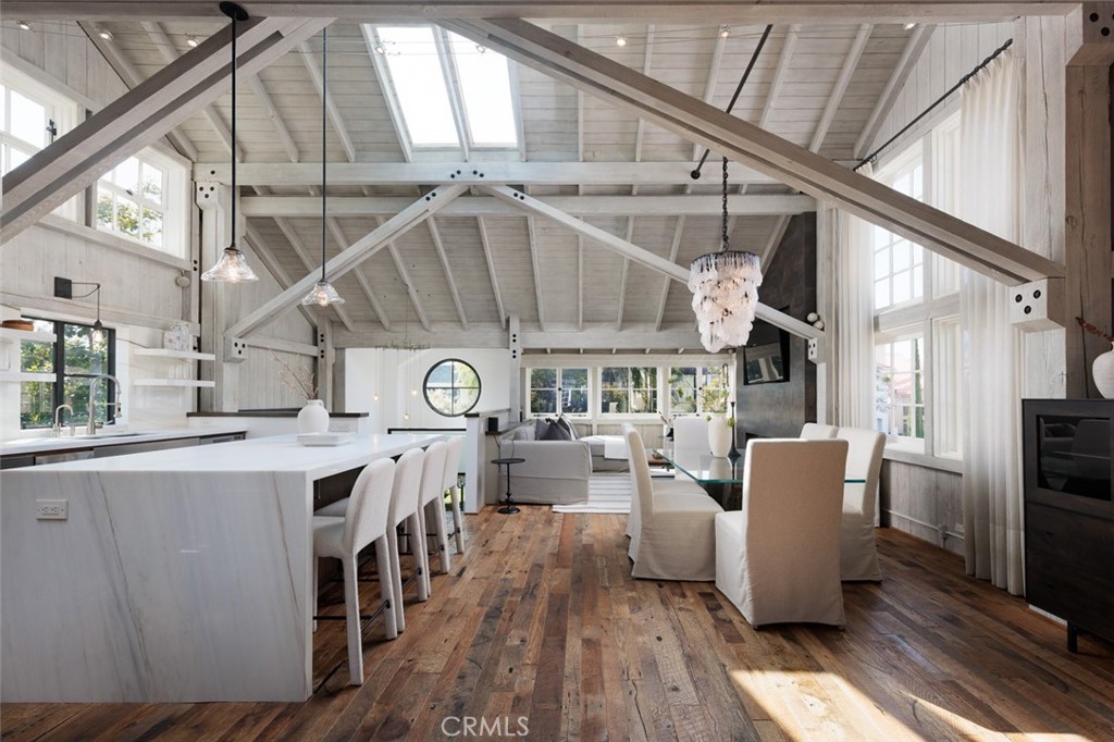 Located on the coveted ocean side of Pacific Coast Highway, this remarkable property offers the rare combination of privacy, versatility, and design in the heart of the Flower Streets. Set on a full lot, the Napa Valley farmhouse-inspired home lives like a true single-family residence with an attached two-car garage, a beautifully landscaped courtyard, and a detached guest house—perfect for rental income, extended stays, live-in help, or a private office.
Originally built by architect Mark Billing and reimagined in 2012, this home seamlessly blends timeless charm with contemporary elegance. The thoughtful floor plan and lush landscaping maximize privacy—an exceptional feature in this vibrant village setting. Just a short stroll to cafés, boutiques, restaurants, and galleries, this home provides coastal living with both luxury and convenience.
The main residence features two bedrooms with en suite bathrooms, a built-in office nook, additional office or sitting room, and laundry on the first level. A dramatic wood-and-glass staircase leads to the open-concept second floor, where beamed trussed ceilings and skylights create a warm, inviting atmosphere. The living, dining, and kitchen areas flow effortlessly, ideal for entertaining or everyday living. The gourmet kitchen features Wolf appliances, white marble island with seating, open shelving, and a walk-in pantry complete with a dumbwaiter. The dining area is lit by a custom chandelier made from vintage cycle chains and hand-blown crystals, while the family room centers around a sleek fireplace, blending rustic charm with modern comfort.
The private guest house mirrors the same high-end finishes and thoughtful design, with its own entrance, eat-in kitchen with Wolf appliances, vaulted ceilings, skylights, and en suite bedroom. Both structures feature vintage barn wood flooring, tying together the home’s cohesive style and craftsmanship.
A shared outdoor deck with built-in BBQ and seating completes the indoor-outdoor lifestyle, all tucked behind privacy-enhancing landscaping. This rare gem offers sophistication, flexibility, and tranquility in one of Corona del Mar’s most desirable locations.