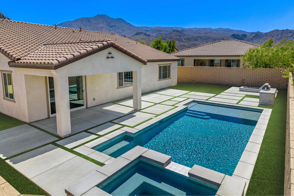 Desert luxury hits a high note at 58229 Coral View Way--an architectural showpiece and the crown jewel of Cantera at Coral Mountain. Set on one of the community's largest lots, this rare 4-bedroom, 3-bath single-story stunner sprawls across 3,114 square feet of refined living, framed by panoramic Coral Mountain views and golden-hour sunsets. A brand-new PebbleTec pool with a raised spillway spa and a built-in outdoor kitchen--complete with grill, beverage fridge, and bar--create an entertainer's paradise, perfect after a day on PGA fairways or the Indian Wells courts. Inside, the chef's quartz-clad kitchen and full KitchenAid suite flow seamlessly into an expansive 829 sq.ft. great room drenched in natural light--ideal for hosting Coachella weekends or BNP Paribas soirees. Dual primary suites with spa-worthy baths, plus two additional guest rooms, offer flexibility and luxury. Fully owned rooftop solar, EV charging, Energy Star construction, HERS42 efficiency, and smart-home wiring deliver sustainability with style. The oversized 3-car tandem garage handles all your gear, and with low $247/month HOA dues, this turnkey gem blends lock-and-leave convenience with resort-level indulgence. Homes with paid solar, dual suites, low HOAs, and Coral Mountain vistas are unicorns--this one just happens to exist.