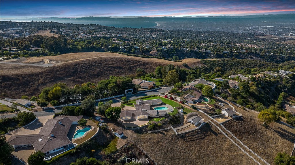 A Rare Cliff May-Designed Equestrian Estate with Unrivaled Views in Rolling Hills. Welcome to your private hilltop retreat, where classic California ranch architecture meets resort-style living. This spectacular 5-bedroom, 5.5-bath estate designed by iconic architect Cliff May is nestled behind the 24/7 guard-gated community of Rolling Hills. Perfectly positioned on one of the best streets in the city, this property offers sweeping, unobstructed views of the Queen’s Necklace, Downtown Los Angeles, and the glittering city lights below. Thoughtfully crafted to capture its breathtaking surroundings, nearly every room in the home frames a panoramic view. Floor-to-ceiling windows fill the formal living and dining rooms with natural light, while marble floors and vaulted ceilings add an air of quiet elegance. The gourmet kitchen opens to an inviting family room, ideal for casual gatherings and seamless indoor-outdoor living. Outside, a sparkling pool and built-in BBQ anchor the spacious entertaining patio—an ideal setting for sunset soirées or weekend relaxation. A detached guest apartment with kitchenette offers comfort and privacy for visitors or multigenerational living. For the equestrian enthusiast, the estate features a barn, corral, and wash area along with the potential to convert the barn to an ADU (buyer to verify with city). With approximately 2 flat acres, the property offers space for a pickleball court, vineyard, orchard, or expanded pasture—bringing endless possibilities to life. Originally selected by the former president of Southern California Edison as the first home site on Buggy Whip Drive, this exceptional lot was chosen for its dramatic 180-degree views and expansive flat pad. The result is a timeless, peaceful setting that feels worlds away yet is just minutes from South Bay beaches, shopping, and dining. Rolling Hills offers a lifestyle unlike any other in Los Angeles: a secluded, equestrian-friendly community with private riding and hiking trails, community tennis courts, and three secured entrances. This one-of-a-kind property is more than a home—it’s a legacy estate ready for its next chapter.